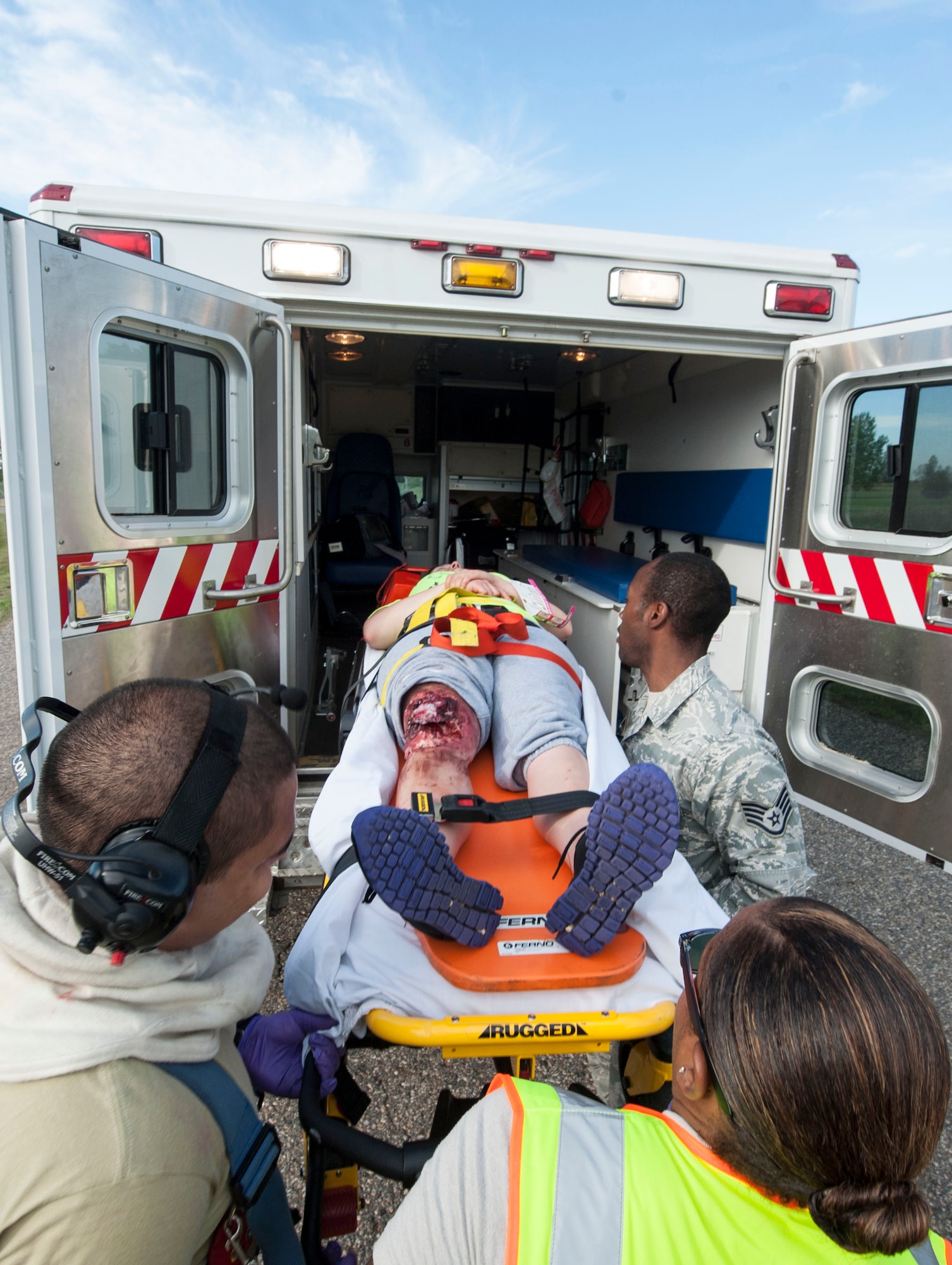 5th Medical Group personnel assist a 5th Civil Engineer Squadron firefighter with loading a simulated amputation victim into an ambulance during an exercise at Minot Air Force Base, N.D., July 22, 2015. The exercise tested the skills of emergency response personnel from a variety of base agencies including firefighters, emergency medical technicians and 54th Helicopter Squadron crew members. (U.S. Air Force photo/Senior Airman Stephanie Morris)