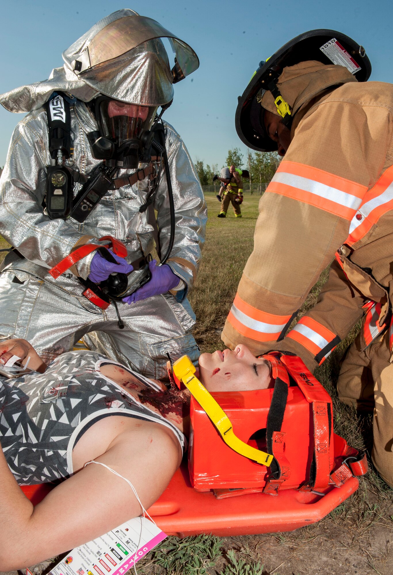Staff Sgt. Symphony Leyk, 5th Security Forces Squadron alarm monitor, is loaded onto a back board by 5th Civil Engineer Squadron firefighters during an exercise at Minot Air Force Base, N.D., July 22, 2015. Leyk had a simulated neck wound which emergency responders had to identify and treat during the exercise. (U.S. Air Force photo/Senior Airman Stephanie Morris)