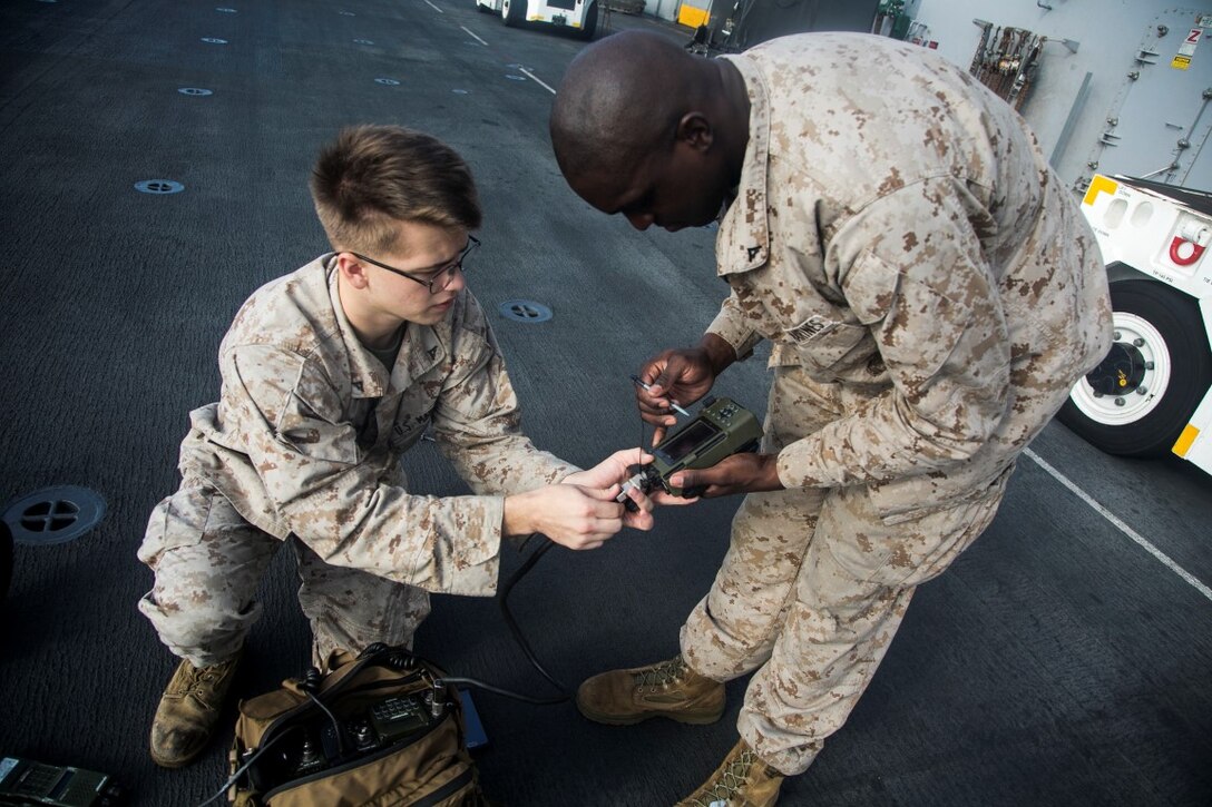 U.S. Marine Lance Cpl. Casey Dawes, left, and Lance Cpl. Derale Burrius perform maintenance checks with their radios on the flight deck of the amphibious assault ship USS Essex (LHD 2). Dawes and Burrius are radio operators with Headquarters and Support Company, Battalion Landing Team 3rd Battalion, 1st Marine Regiment, 15th Marine Expeditionary Unit (MEU). Elements of the 15th MEU, based out of Camp Pendleton, California, and embarked aboard the Essex, are conducting naval operations in the 6th Fleet area of operations in support of U.S. national security interests in Europe and Africa. (U.S. Marine Corps photo by Cpl. Anna Albrecht/Released)