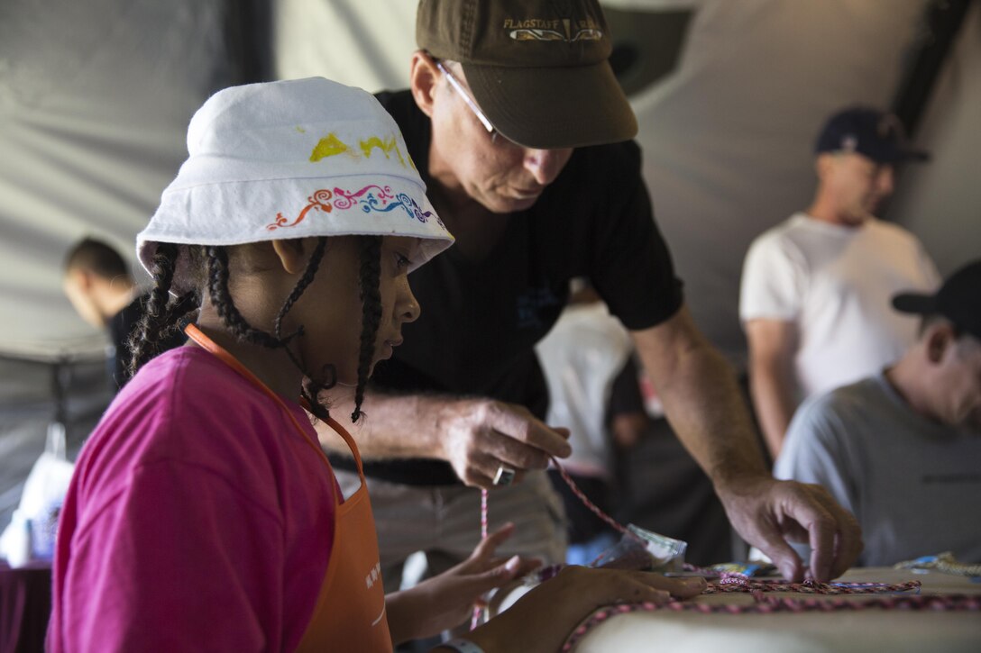 Amaya Lewis, grandaughter of Vandra Lewis, Navy veteran and San Diego native, makes a bracelet with the help of Gary Elfman, a volunteer with Alvarado and Paradise Valley Hospitals at the San Diego Stand Down for Homeless Veterans and their families, July 18. Marine Wing Support Squadron 373 from Marine Corps Air Station Miramar transported, set-up and maintained the tents and other equipment used during the stand down. (U.S. Marine Corps photo by Sgt. Lillian Stephens)
