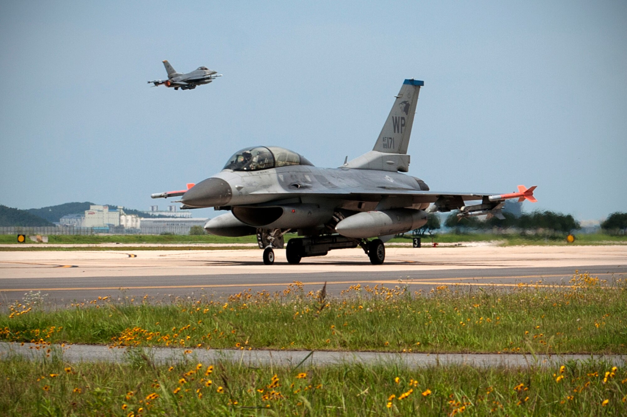 A U.S. Air Force 35th Fighter Squadron F-16 Fighting Falcon taxis on the Kunsan Air Base runway as an 80th Fighter Squadron F-16 Fighting Falcon takes off during Exercise Buddy Wing 15-4 at Kunsan Air Base, Republic of Korea, July 16, 2015. The five-day quarterly operational readiness exercise enhanced strategic capabilities at Kunsan by generating combat airpower in a simulated chemical, biological, radiological, nuclear and high-yield explosive environment. (U.S. Air Force photo by Senior Airman Katrina Heikkinen/Released)