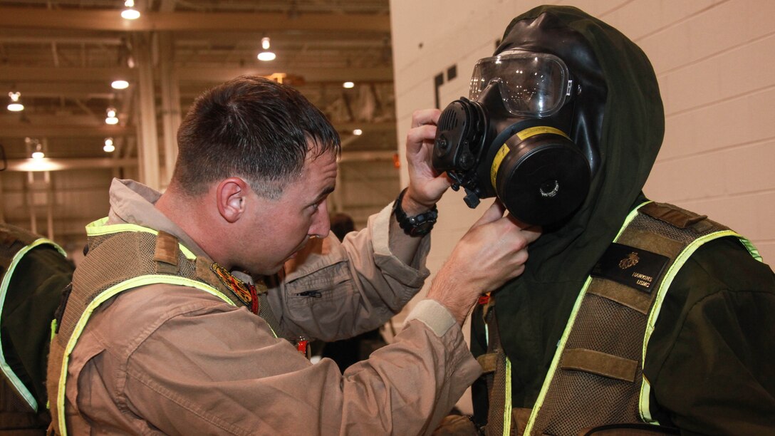 Sergeant Austen Clark, the hot zone controller for the Search and Extraction Platoon, helps one of his Marines fasten and secure his gas mask before completing the final exercise of the afternoon during Exercise Scarlet Response 2015 at Guardian Centers in Perry, Georgia, July 21. The hot zone is the area where an incident occurs. Clark makes sure he keeps accountability of everything that goes on when his Marines go in and search a building, such as their gear, if there are any casualties inside or if there are any further issues besides what they already know. 