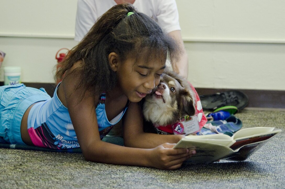 Brianna Torbert, 10, gets affection from therapy dog Molly, an 8-year-old miniature Australian shepherd during the Reading to Dogs event at the base library, July 22, 2015. Molly is certified with the Reading Education Assistance Dogs program from Intermountain Therapy Animals, a nonprofit organization based in Salt Lake City. Molly, and her handler, Angie McGaffin, a board member of nonprofit organization, Tails of Aloha, visit various locations on the island to provide therapy for people. (U.S. Marine Corps photo by Kristen Wong/Released)