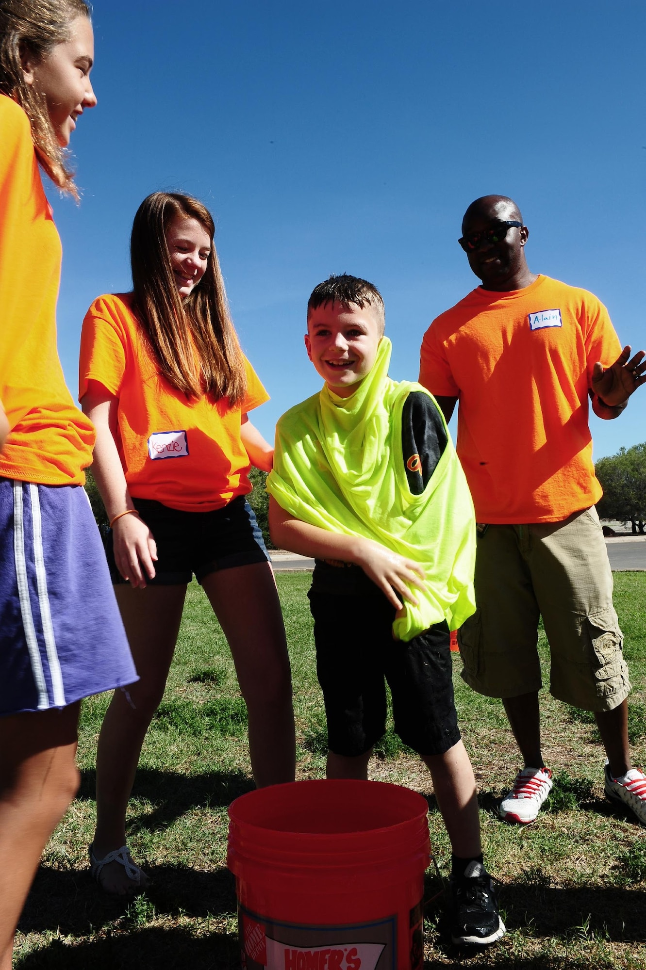 Volunteers in orange T-shirts lead a game where participants have to race to put on a soaking wet shirt at the chapel’s vacation bible school July 21. The outdoor challenge station was one of many stations that volunteers work. (U.S. Air Force photo by Amn Randahl J. Jenson)