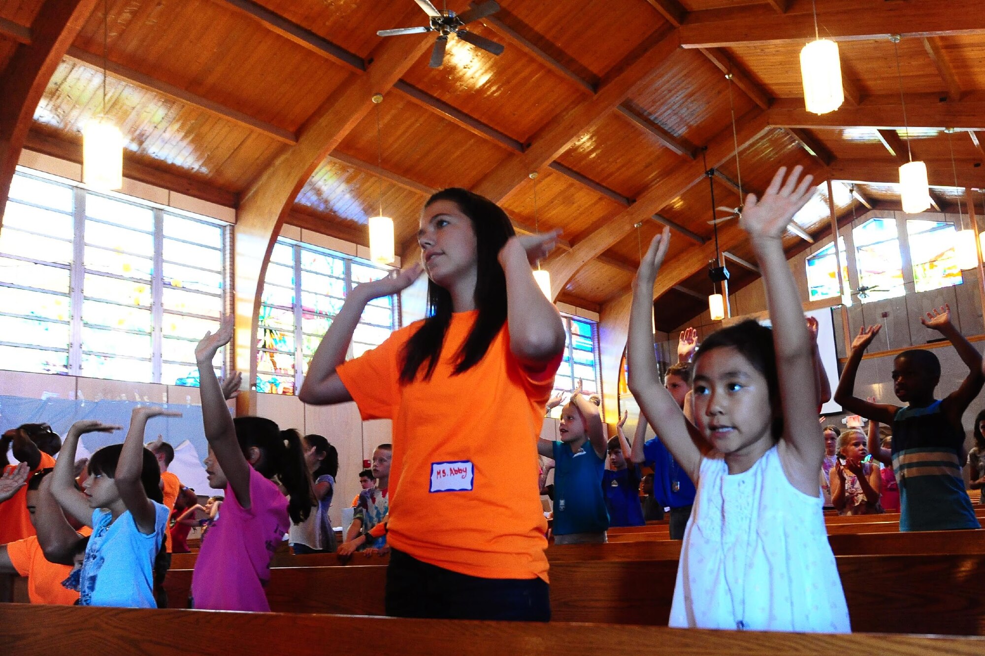 Abby L. Sherwood, a volunteer, helps lead children in a sing-along at the chapel’s vacation bible school July 21. Volunteers play music videos with characters performing dance moves on the screens inside the chapel to lead children in worship music. (U. S. Air Force photo by Amn Randahl J. Jenson)