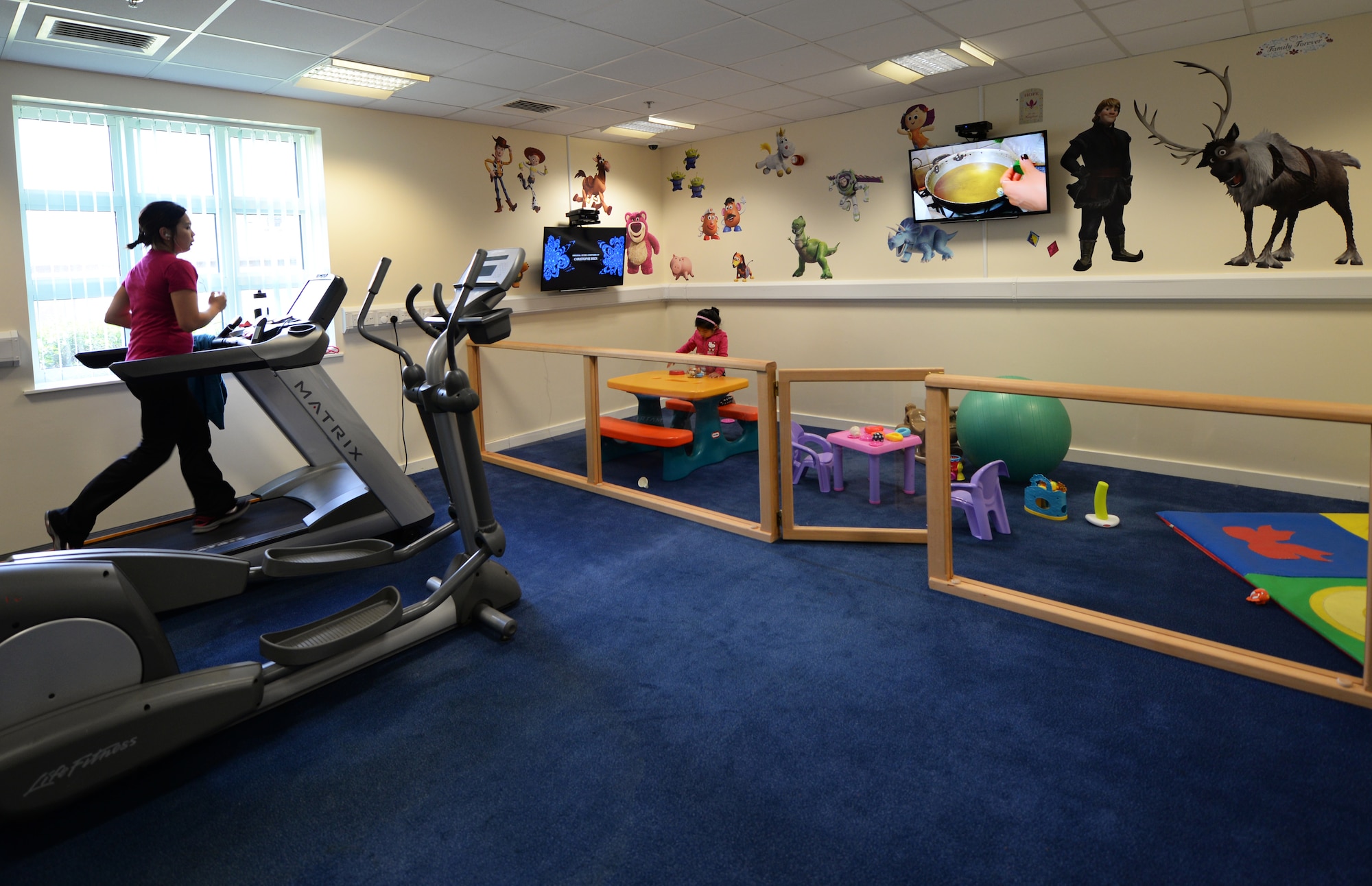 The Family Workout Zone provides an opportunity for a Liberty spouse to workout while her daughter plays safely at Royal Air Force Lakenheath, England, May 19. The family-friendly workout area is one of several updates to the Lakenheath Fitness Center. The fitness center facilities are now available 24/7 by card reader. (U.S. Air Force photo by 2nd Lt. Kellie Rizer/Released)