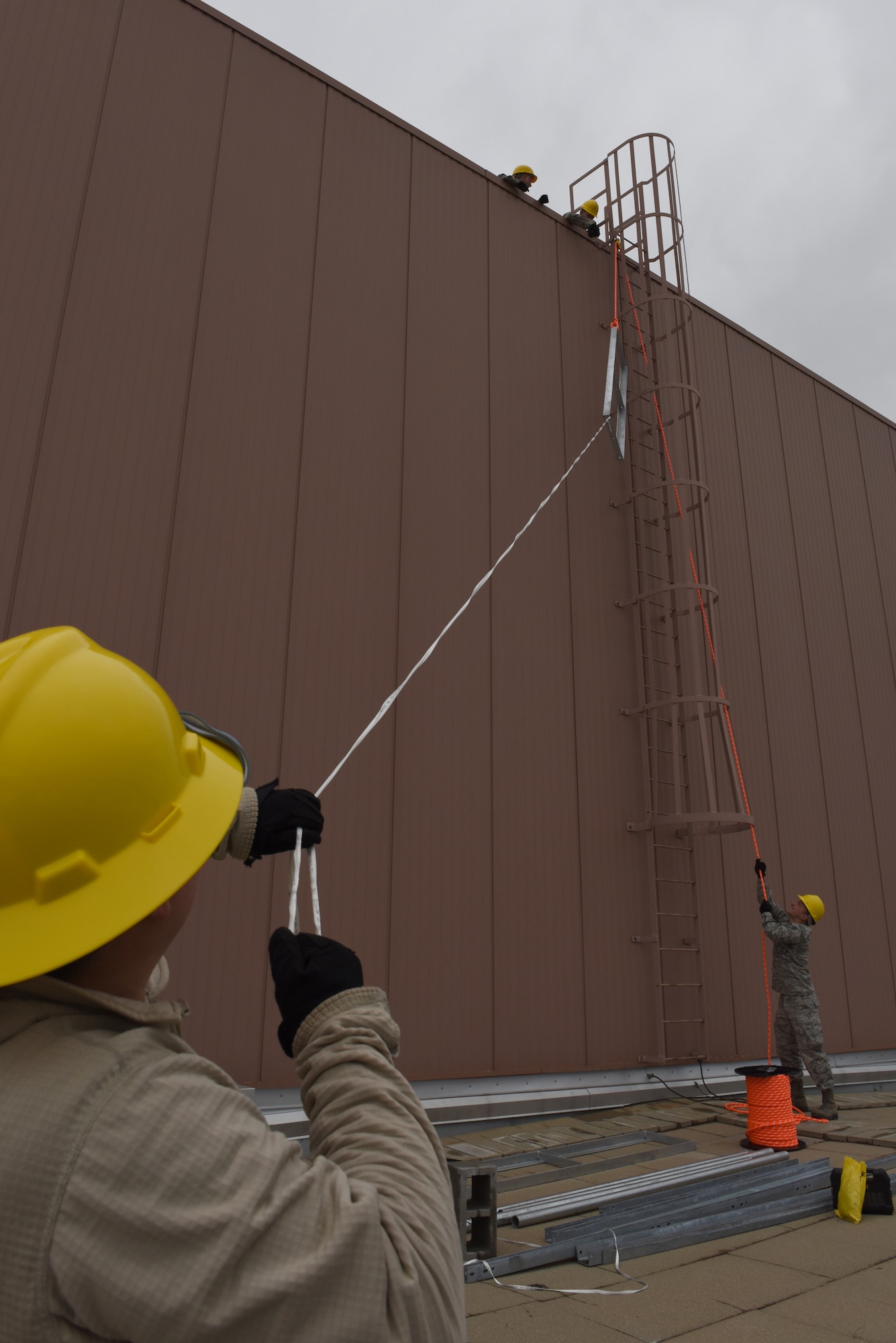 Senior Airman Heather Holmes, cable and antenna systems technician, and Staff Sgt. Eric Bauman radio frequency technician, both of the 211th Engineering Installation Squadron, lift a piece of non-penetrating antenna tripod base to the third level of a hanger roof of the 168th Air Refueling Wing, Eielson Air Force Base, Fairbank, Alaska. Holmes and Bauman are part of an eight-person team working on the antenna grounding projects as part of Exercise Frosty Spear, July 13-24, 168th Air Refueling Wing, Eielson Air Force Base, Fairbanks, Alaska. (U.S. Air National Guard photo by Staff Sgt. Claire Behney)