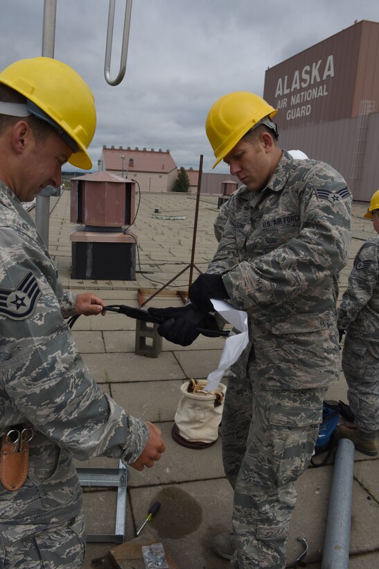 Staff Sgt. Eric Bauman, radio frequency technician, and Senior Airman Matt Monteleone, cable and antenna systems technician, both of the 211th Engineering Installation Squadron apply butyl to weatherproof antenna cables on the roof of a hanger of the 168th Air Refueling Wing, Eielson Air Force Base, Fairbanks, Alaska. The 211th EIS is participating in Exercise Frosty Spear, July 13-24, where they're completing communication room grounding, video distribution, paging, and antenna grounding projects. (U.S. Air National Guard photo by Staff Sgt. Claire Behney)