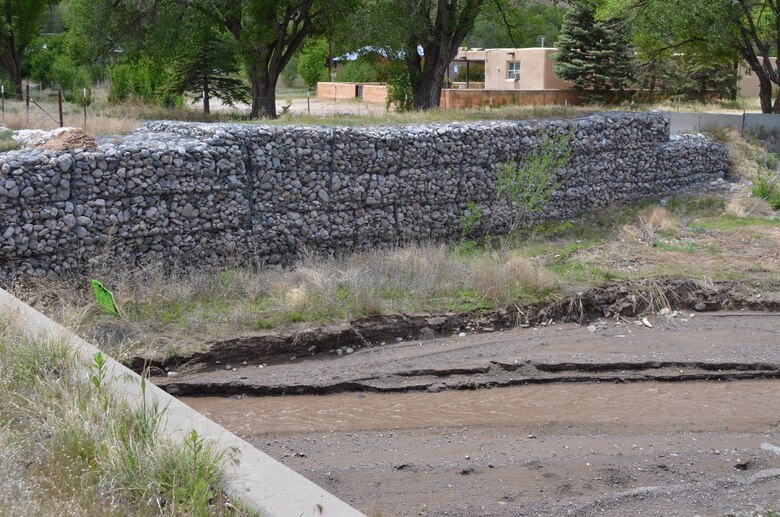 As Climate Changes, Santa Clara Strives To Become Resilient To Worsening Fires, Floods: Rock-filled gabion baskets line the Santa Clara Creek where it flows under a state road in Santa Clara Pueblo. High flows of water from the burn scar in Santa Clara Canyon and the watershed of Santa Clara Creek threaten the village, and the mesh-and-rock gabion structures assist with flood control. Courtesy Elizabeth Lockyear/U.S. Army Corps of Engineers, Albuquerque District