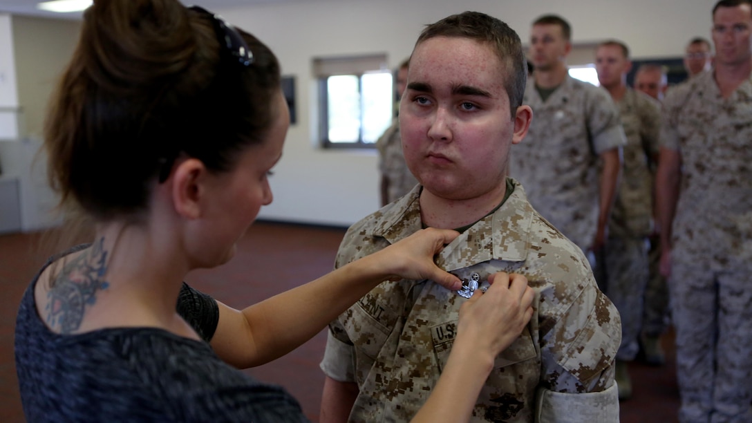 James Gallant, a young man diagnosed with brain cancer, is pinned with an Explosive Ordnance Disposal technician badge by his mother Sarah Silverstein, before Marines of 1st EOD Company, 1st Marine Logistics Group, aboard Camp Pendleton, Calif., July 25, 2015. Collaborating with the Make-A-Wish Foundation, 1st EOD helped James experience what being an EOD technician is like by giving him a tour through their library of ordnance and EOD tools, teaching him to operate the TALON bomb disposing robot and presenting him with his own desert utilities and EOD badge.