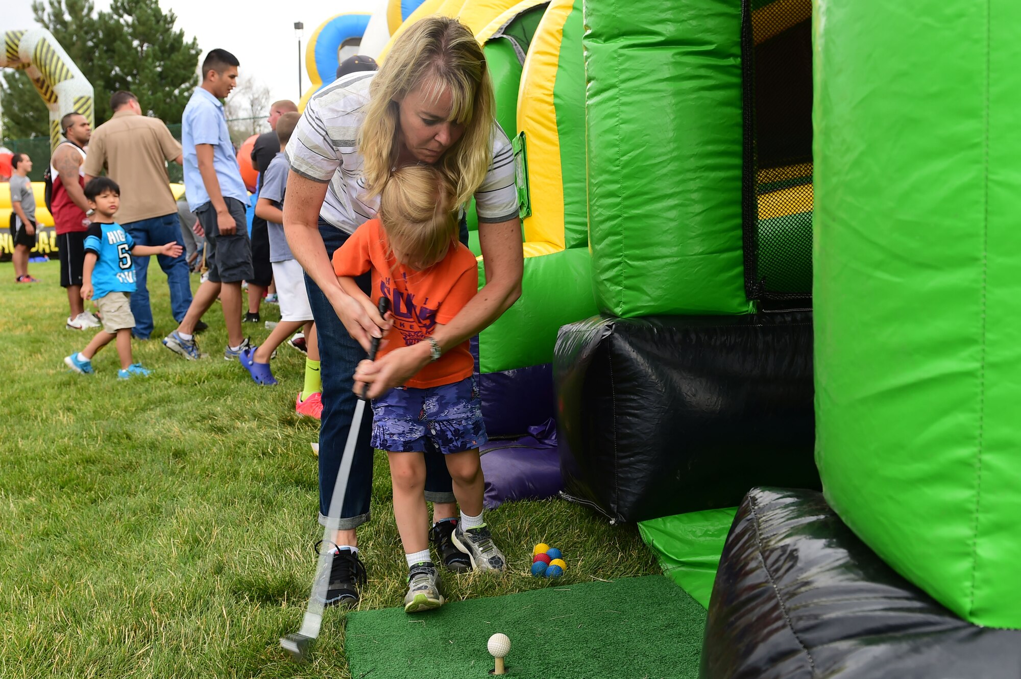 A mother helps her daughter hit a golf ball during FunFest July 24, 2015, at Buckley Air Force Base, Colo. FunFest is an annual base-wide event that includes family-friendly games and activities, community involvement and local business sponsors. (U.S. Air Force photo by Airman 1st Class Luke W. Nowakowski/Released)