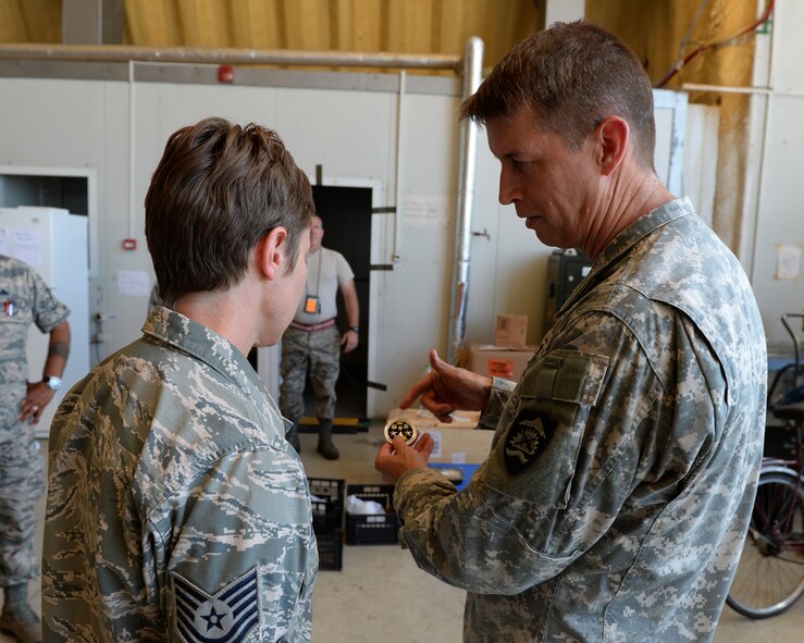 U.S. National Guard Maj. Gen. Daniel Hokanson, Oregon National Guard Adjutant General, describes his coin to an Airman that he will coin during a base tour at Campia Turzii, Romania, July 22, 2015. Hokanson visited the 123rd Expeditionary Fighter Squadron during their theater security package deployment to Campia Turzii. The visit allowed Hokanson to pass along information from home, answer questions and learn more about their mission in Romania. More than 200 Airmen from the 142nd Fighter Wing, Oregon Air National Guard, Portland, Oregon, are training with the Romanian air force as part of a European theater security package of F-15C Eagles deployed to Romania. (U.S. Air Force Senior Airman Dylan Nuckolls/Released)