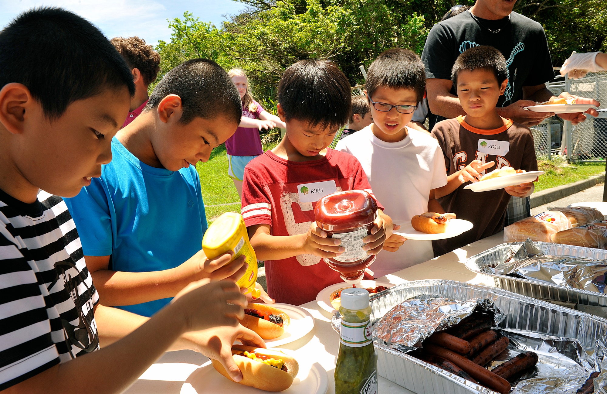 Japanese children from Chatan Town elementary schools, enjoy hotdogs for lunch at the Youth Center during a visit on Kadena Air Base, Japan, July 23, 2015. During the visit, Japanese and American children played ping pong, and other games, and ate an American style lunch together in an effort to learn more about American culture and language. (U.S. Air Force photo by Naoto Anazawa)