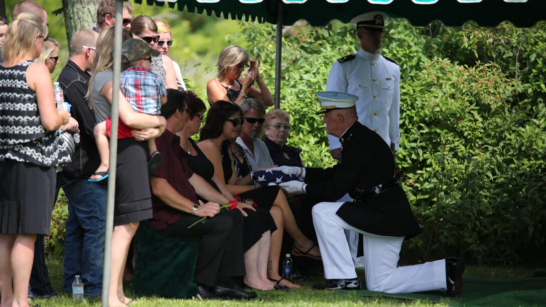 Lt. Gen. Richard P. Mills, commander of Marine Forces Reserve, presents a folded flag to the widow of Sgt. Carson Holmquist, a motor transport maintenance chief with Battery M, 3rd Battalion, 14th Marine Regiment, 4th Marine Division, Marine Forces Reserve, during his funeral July 25, 2015 in Grantsburg, Wisconsin. Holmquist, along with three other Marines and a sailor, was killed in an attack at the Naval Operation Support Center and Marine Corps Reserve Center in Chattanooga, Tennesee July 16, 2015. Marines, family, friends and the community of Grantsburg gathered to honor the memory and sacrifice of Holmquist and his fallen brothers-in-arms.