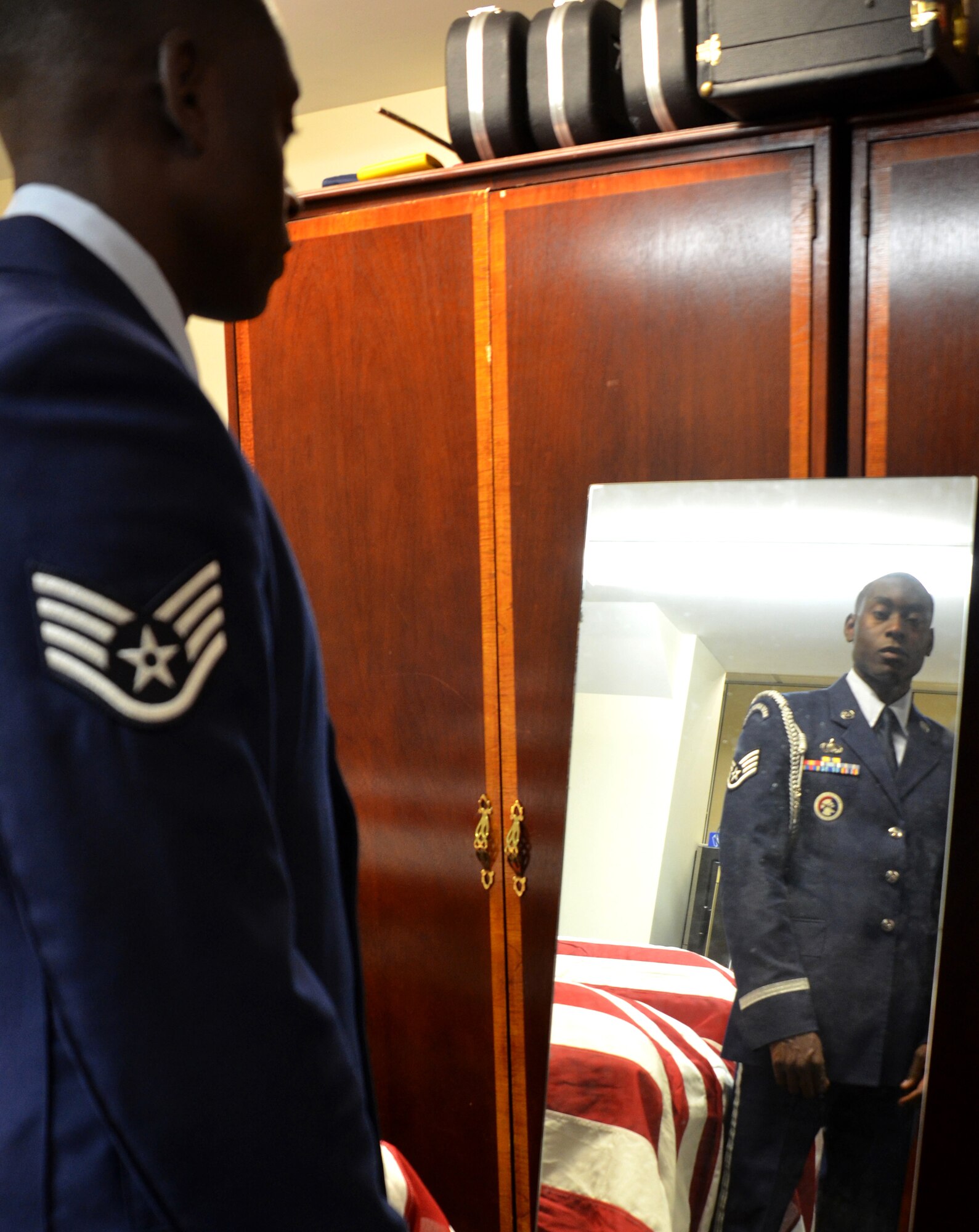 Staff Sgt. Abdul Addy looks himself over in the mirror of the dressing room of the Westover Honor Guard. He is the NCOIC of training of the Westover Honor Guard, which has performed at a staggering amount of over 400 funerals this year alone.