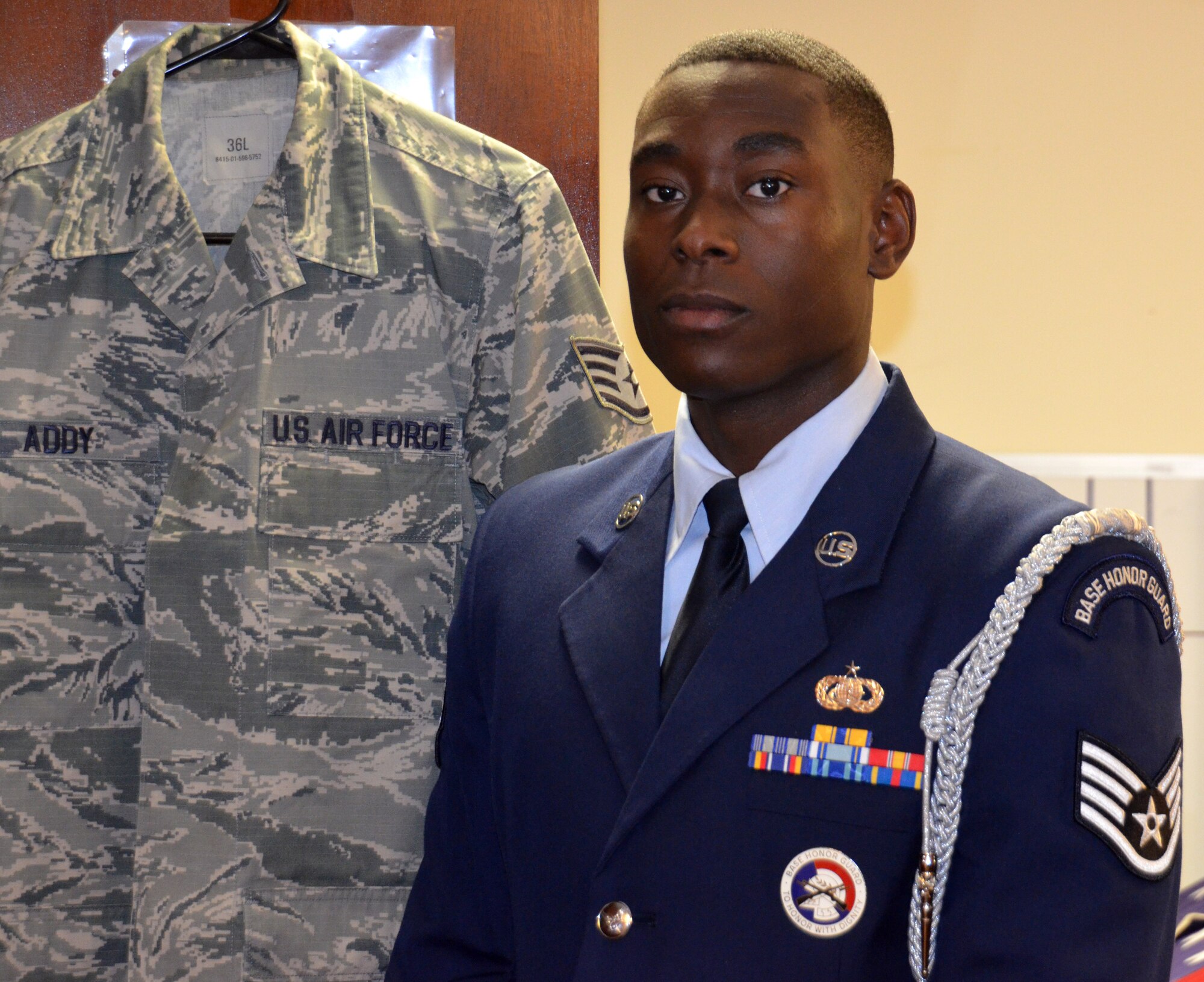 Staff Sgt. Abdul Addy takes a moment to pose next to his ABUs in dressing room of the Westover Honor Guard. He is the NCOIC of training of the Westover Honor Guard, which has performed at a staggering amount of over 400 funerals this year alone.