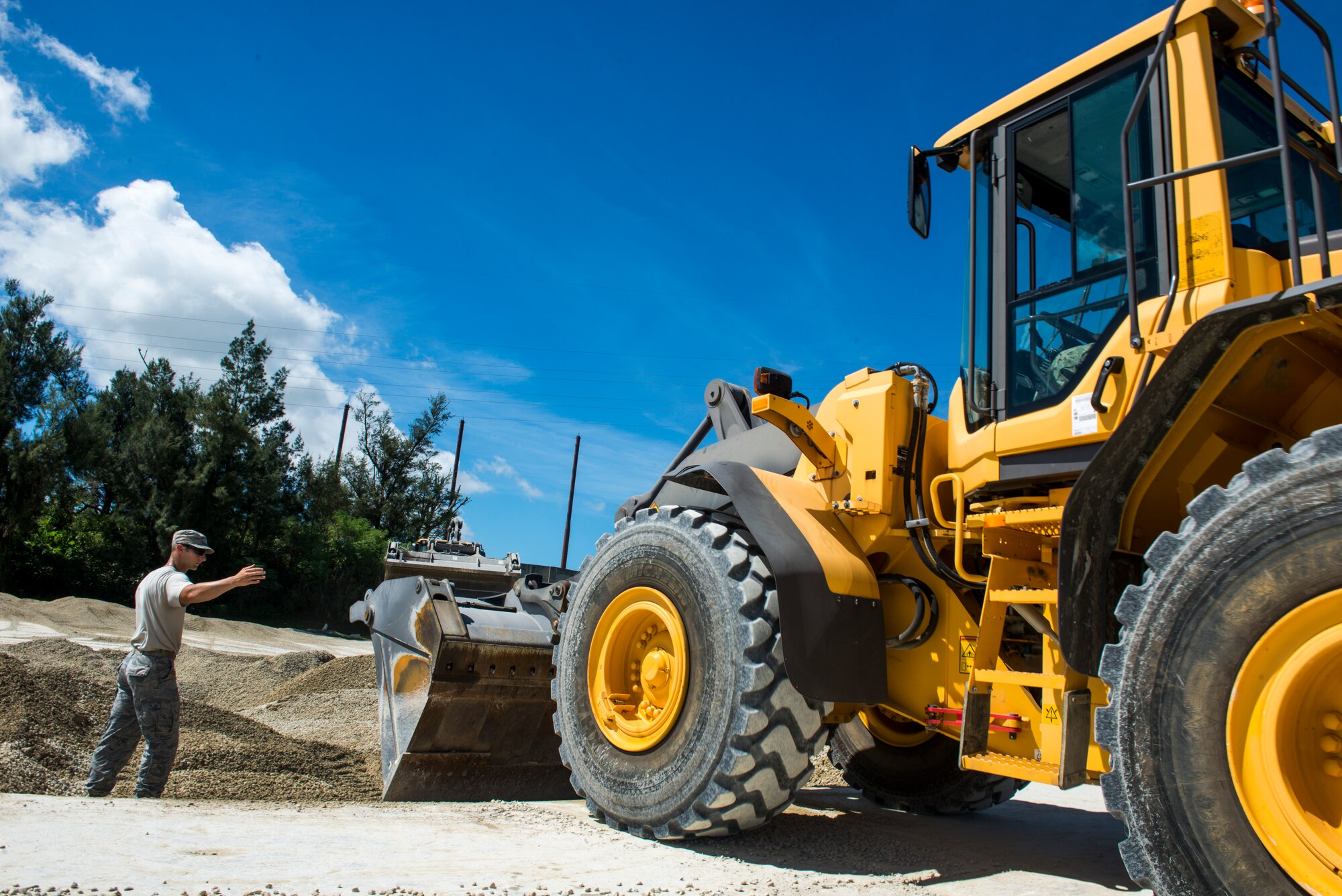 A U.S. Air Force Airman from the 18th Civil Engineer Squadron guides a U.S. Navy Sailor from Naval Mobile Construction Battalion 5 as he pushes debris into a crater during joint airfield damage repair training on Kadena Air Base, Japan, July 23, 2015. The training gave U.S. Air Force and Navy participants the opportunity to gain familiarity with one another while practicing skills they could potential implement in a wartime environment. (U.S. Air Force photo by Staff Sgt. Maeson L. Elleman)