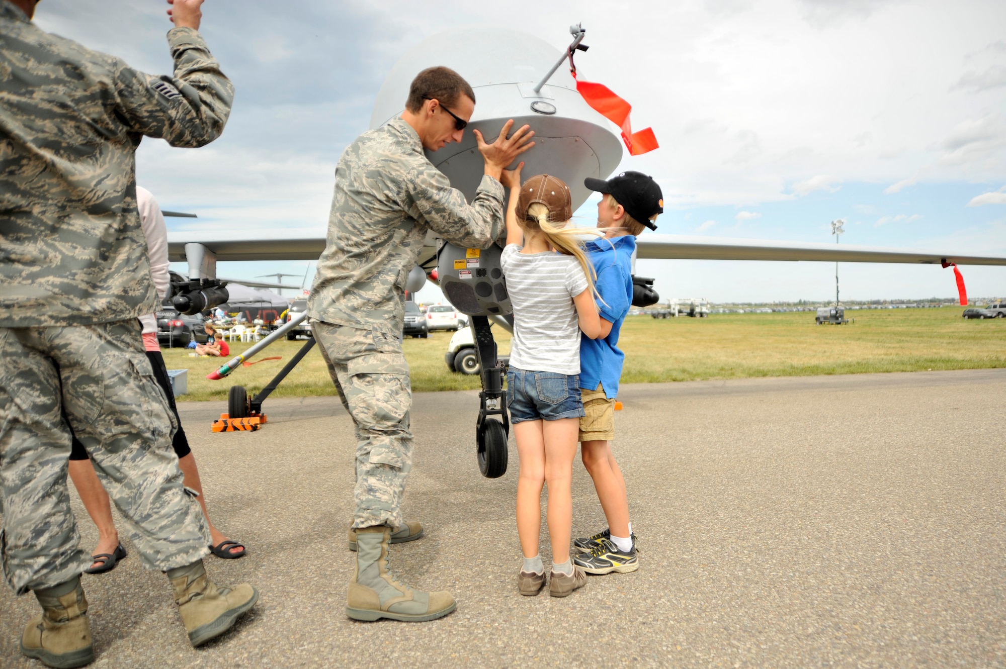 2nd Lt. Joel, 11th Reconnaissance Squadron chief of intelligence, shows Katelynn and Carter Konynenbelt how well the MQ-1 Predator is balanced by lifting the nose of the aircraft at the 2015 Lethbridge International Airshow July 25, 2015, in Lethbridge Canada. Spectators were able to see and touch the aircraft as well as ask the crew questions. (U.S. Air Force photo by Airman 1st Class Christian Clausen/Released)
