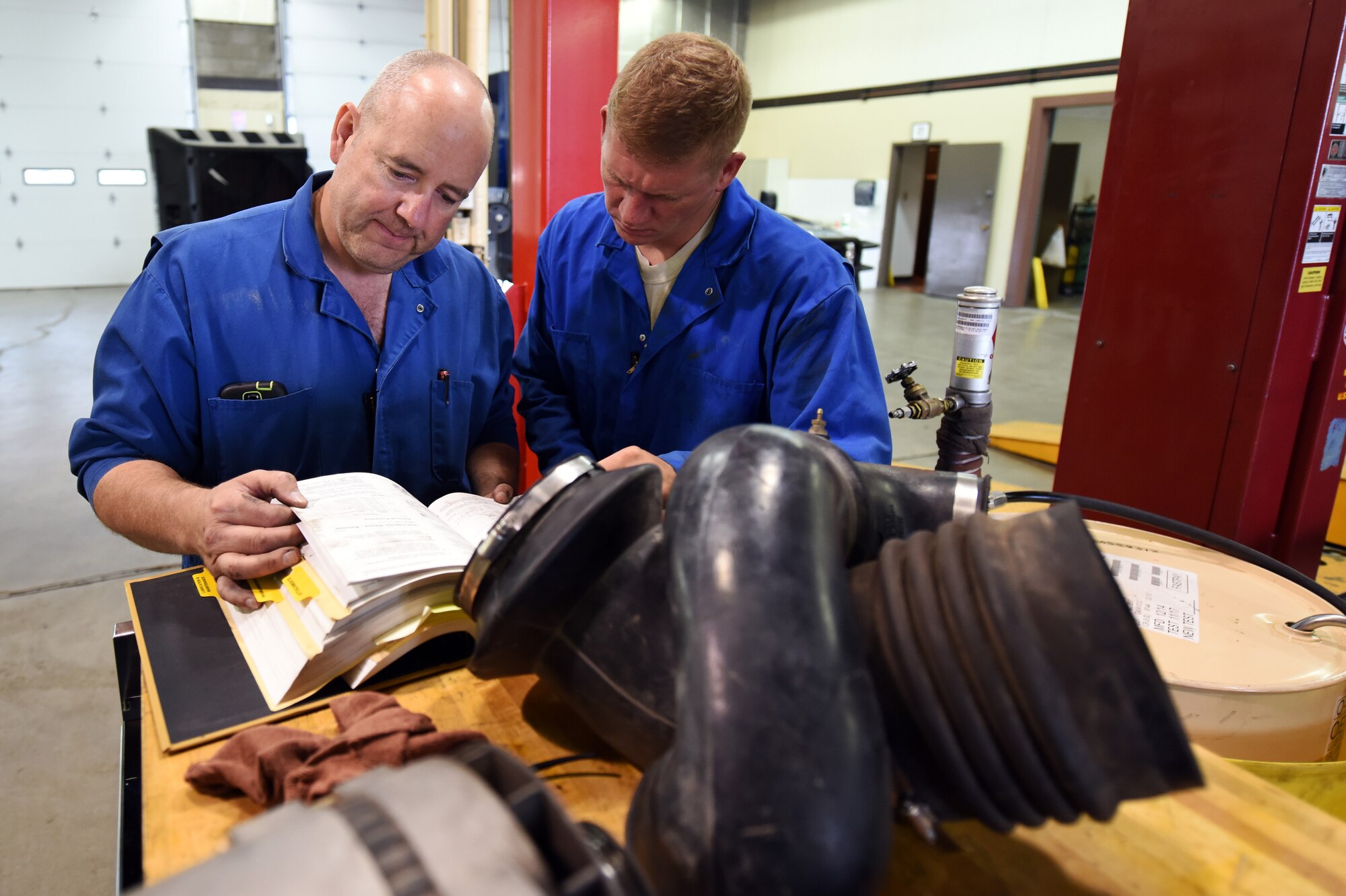 Bob Anderson and Senior Airman Jason Brown, 341st Logistics Readiness Squadron truck and tractor shop vehicle mechanics, review a technical order for procedures to remove injectors on a maintenance van engine July 27, 2015, at Malmstrom Air Force Base, Mont. The 341st LRS truck and tractor maintenance shop maintains all semi trucks and trailers on base. (U.S. Air Force photo/Chris Willis)