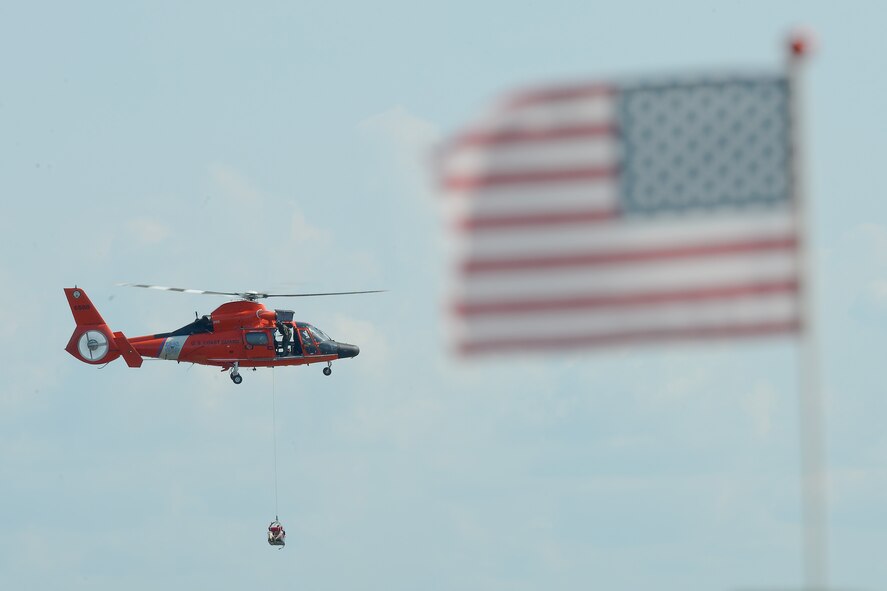An American flag flying on the beach partially frames a U.S. Coast Guard HH-65D Dolphin helicopter that practices hoisting members of the 436th and 512th Airlift Wings from the Delaware Bay during water survival refresher training conducted by the 436th Operations Support Squadron Survival, Evasion, Resistance and Escape Operations July 17, 2015, near Dover Air Force Base, Del.  Team Dover C-5M Super Galaxy and C-17A Globemaster III aircrew are required to undergo refresher training every three years. (U.S. Air Force photo/Greg L. Davis)
