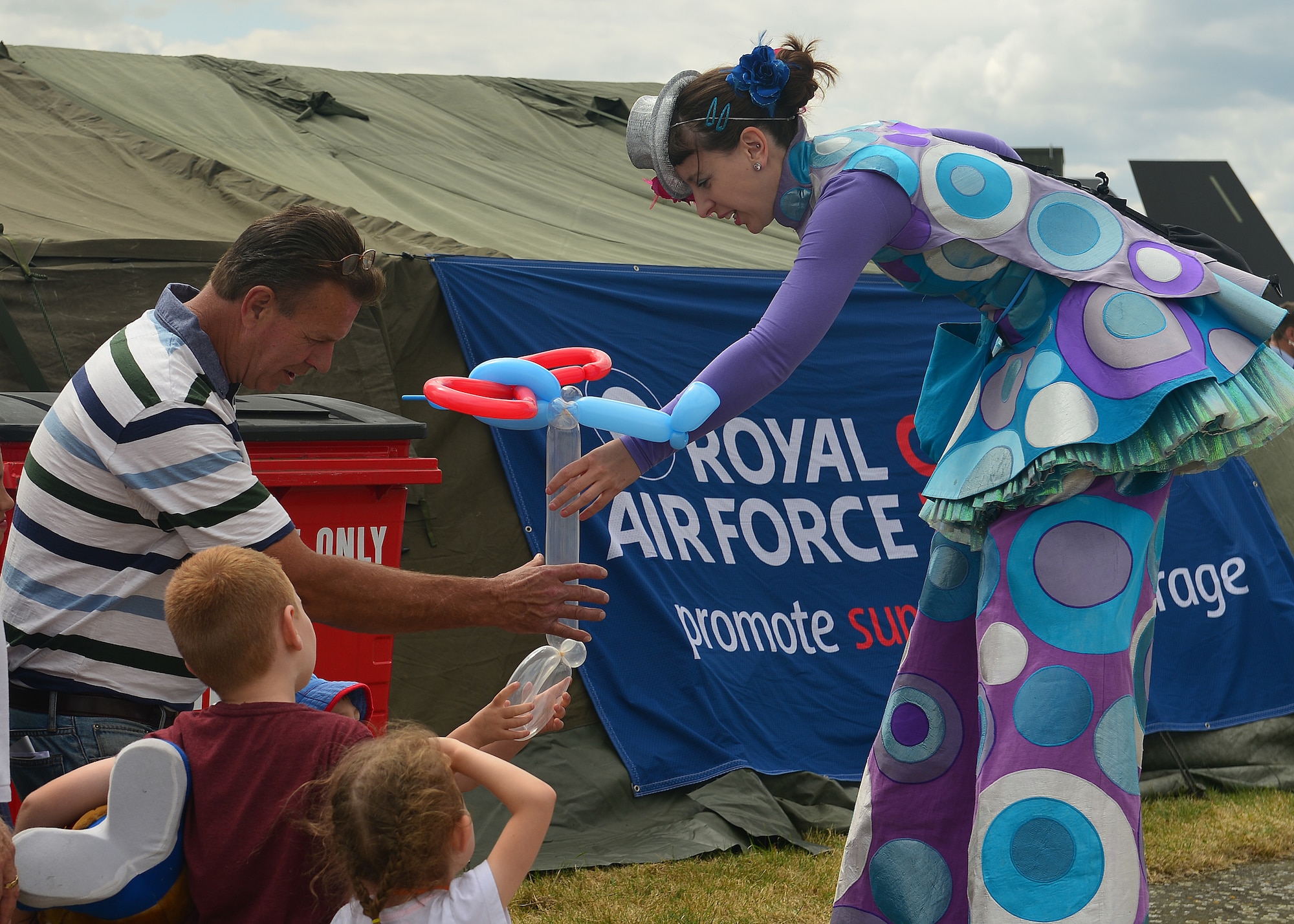 Purdy, on the stilts, gives a boy an airplane balloon during the Families and Friends Day at Royal Air Force Marham, England, July 23, 2015. The event celebrated the 75th Battle of Britain anniversary and welcomed Airmen from RAFs Marham, Lakenheath and Mildenhall, as well as their families and local dignitaries to enjoy a day off. (U.S. Air Force photo by Staff Sgt. Stephanie Longoria/Released)