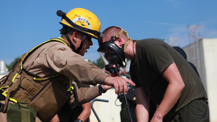 Private First Class Eric Mahoney, a Marine with the Decontamination Platoon, helps a Marine take off his gas mask while also pointing him in the direction of where to go next during the 36-hour continuous operation as part of Exercise Scarlet Response 2015 at Guardian Centers in Perry, Georgia, July 23. When the gas mask is taking off, a Marine must hold his or her breath until they cross a liquid contamination line, which is about 5-10 feet from where they take off the gas mask. 
