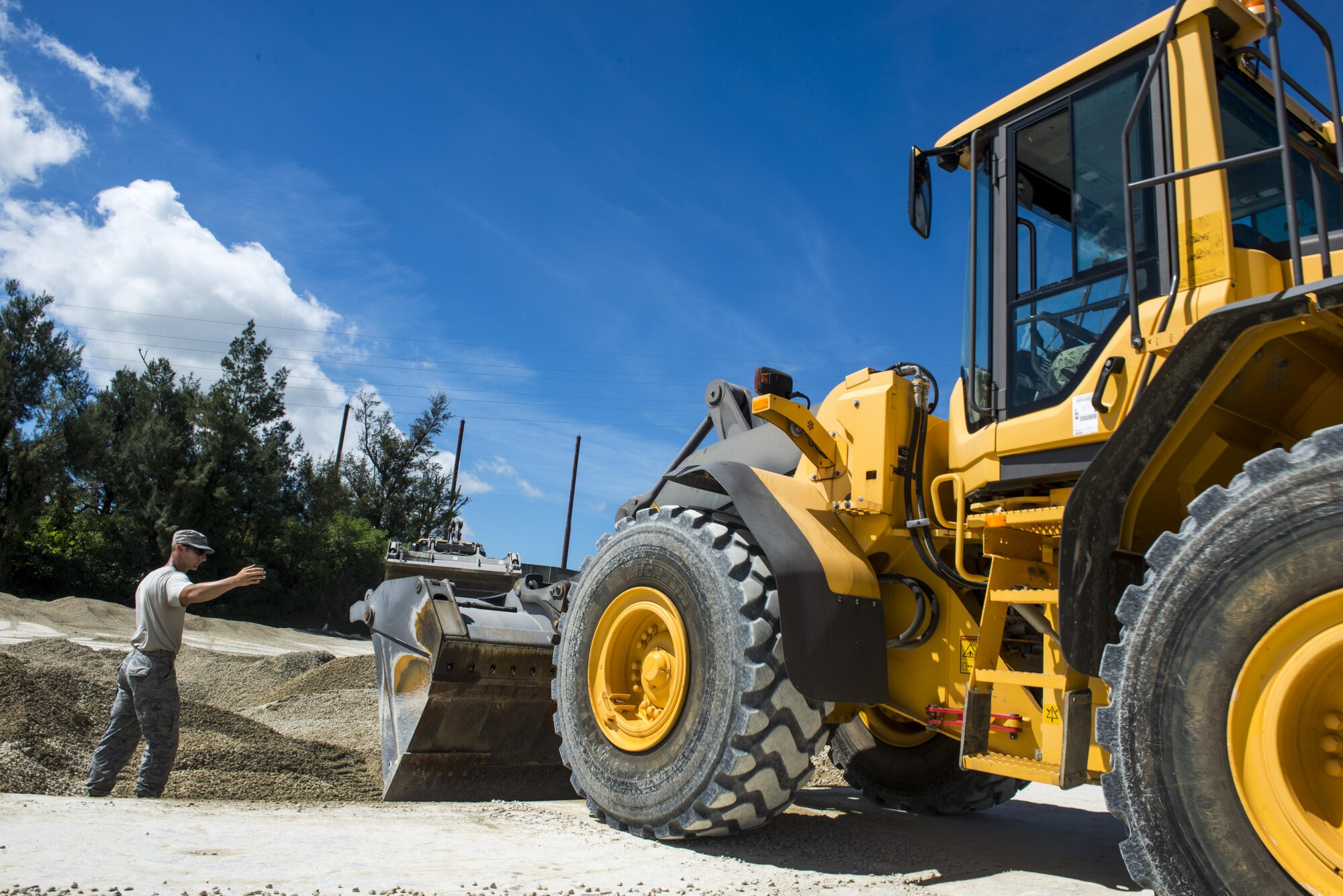 A U.S. Air Force Airman from the 18th Civil Engineer Squadron guides a U.S. Navy Sailor from Naval Mobile Construction Battalion 5 as he pushes debris into a crater during joint airfield damage repair training on Kadena Air Base, Japan, July 23, 2015. The training gave U.S. Air Force and Navy participants the opportunity to gain familiarity with one another while practicing skills they could potential implement in a wartime environment. (U.S. Air Force photo by Staff Sgt. Maeson L. Elleman/Released)
