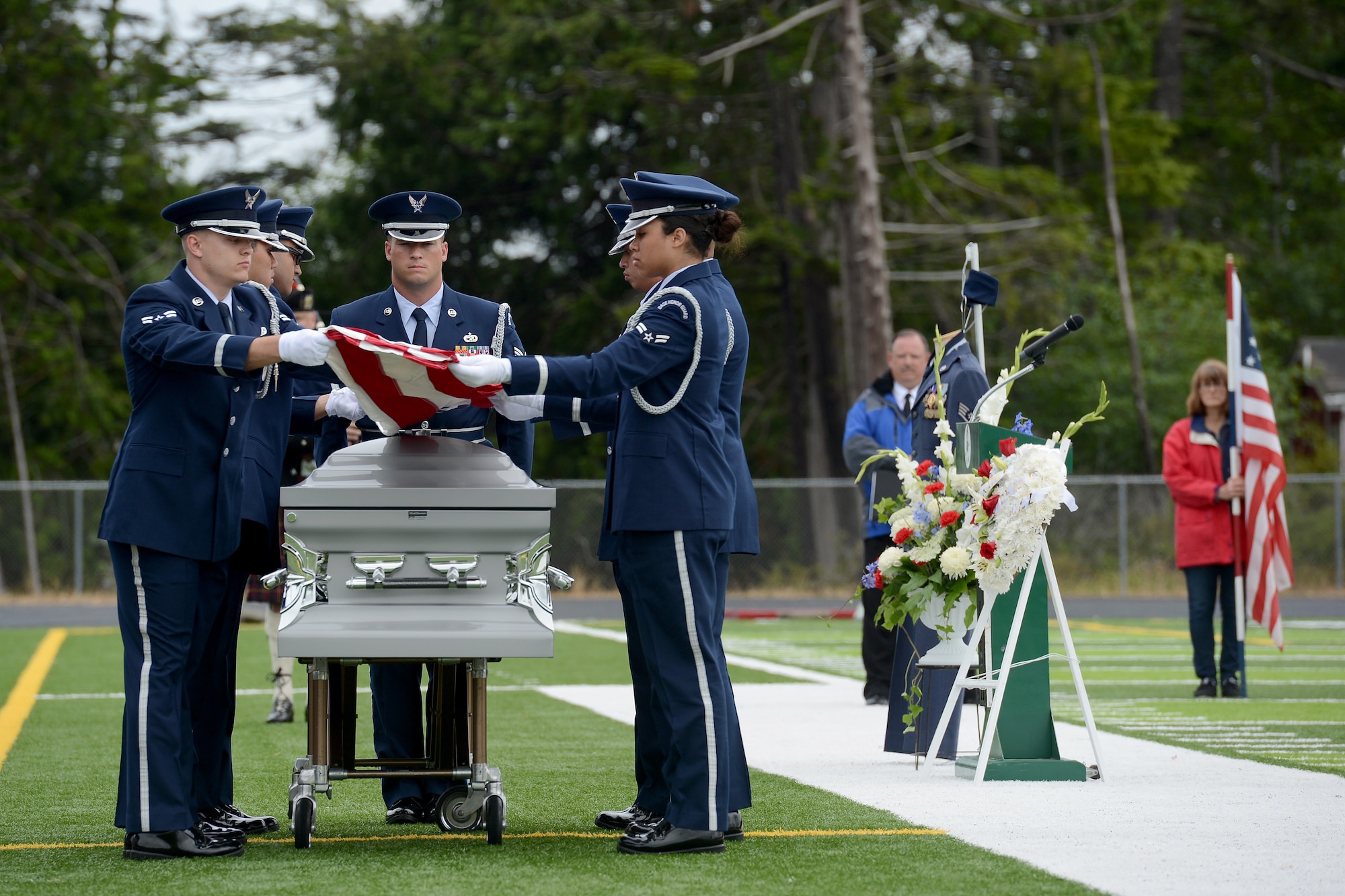 The McChord Field Honor Guard pallbearer team unfolds a flag above a casket July 25, 2015, during an active duty honors ceremony at Waldport High School, Ore. Retiring the casket was the last part of the ceremony before placing the casket into the hearse. (U.S. Air Force photo/Airman 1st Class Keoni Chavarria)