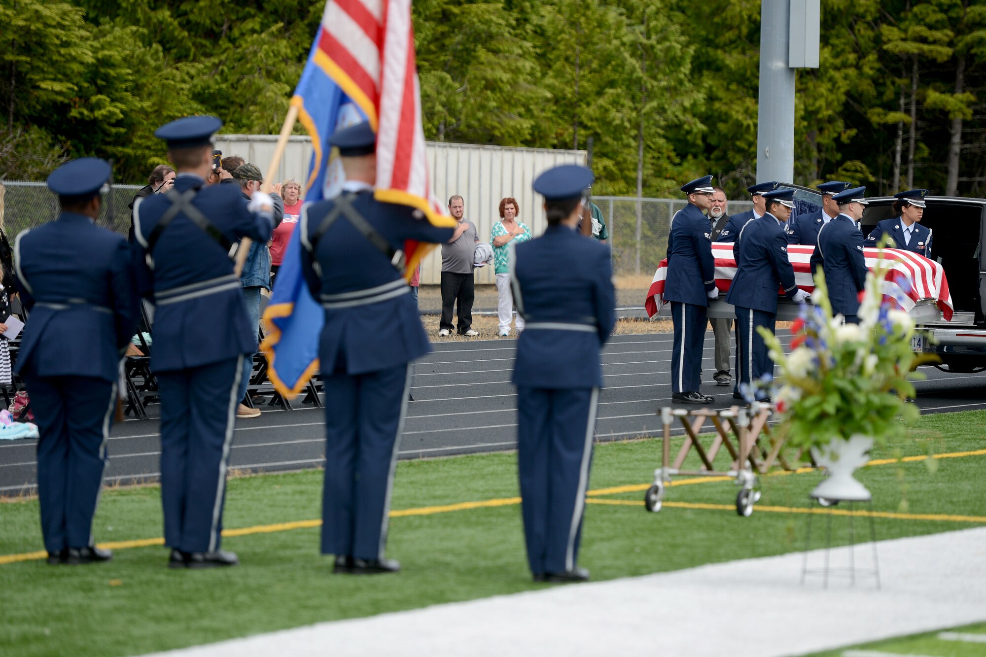 Members from the McChord Field Honor Guard pallbearer team (right), carry a casket, while the color guard team presents the colors July 25, 2015, during an active duty honors ceremony at Waldport High School, Ore. The ceremony honored Tech. Sgt. Hugh Sherburn, an airborne radio communications analyst who was missing in action during his tour in the Vietnam War. (U.S. Air Force photo/Airman 1st Class Keoni Chavarria)