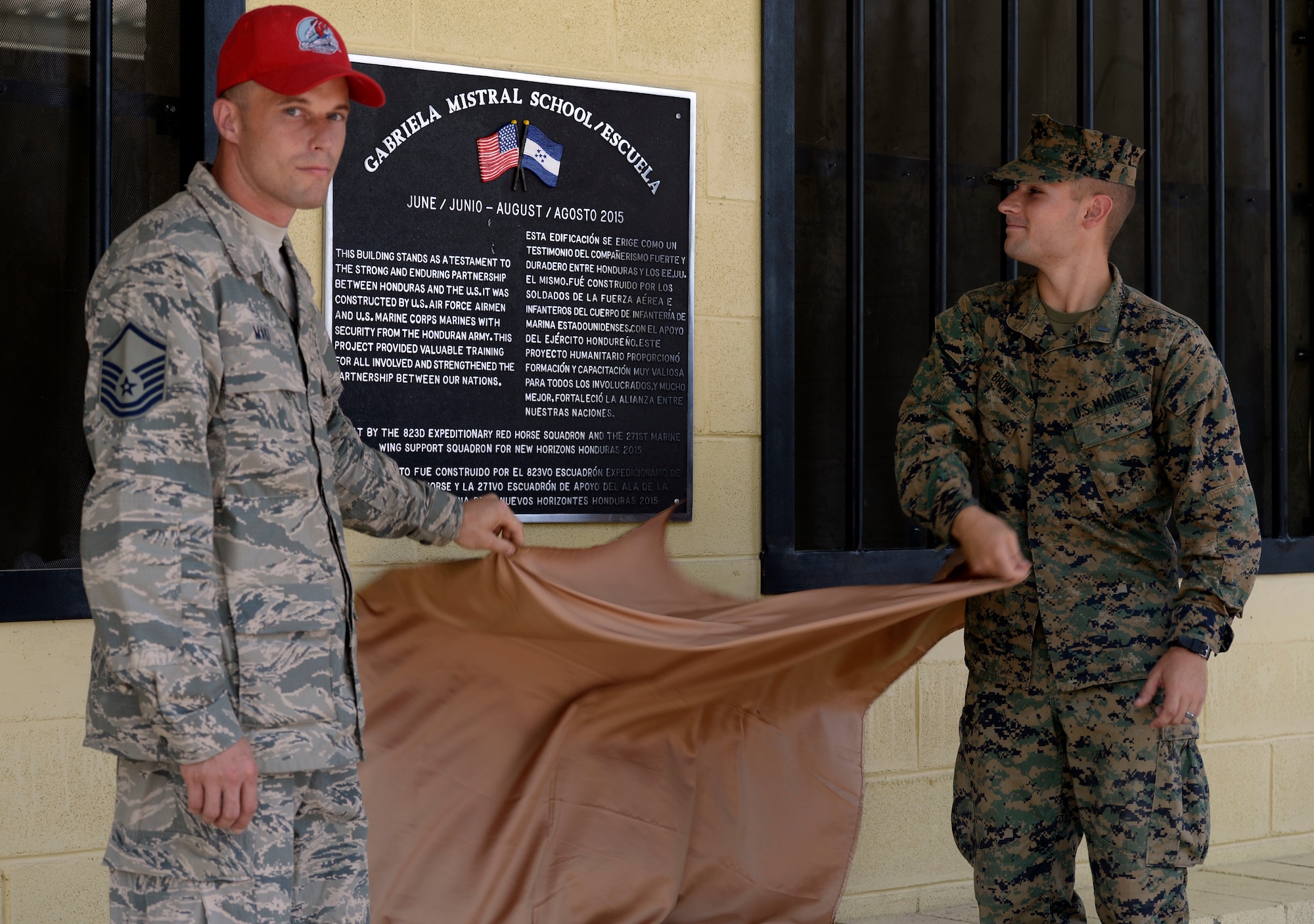 U.S. Air Force Master Sgt. Isaiah Maki, 823rd Expeditionary RED HORSE Squadron project manager, out of Hurlburt Field, Fla. and U.S. Marine Corps 1st Lt. Robert Brown, a combat engineering officer and construction site officer in charge with the 271st Marine Wing Support Squadron, out of Marine Corps Air Station Cherry Point, N.C., unveil the dedication plaque for the new two-classroom schoolhouse at the Gabriela Mistral school in Ocotes Alto, Honduras, July 28, 2015, during a ribbon-cutting ceremony to official open the building. The event marked the official opening of the building which was one of the key projects as part of the New Horizons Honduras 2015 training exercise taking place in and around Trujillo, Honduras. New Horizons was launched in the 1980s and is an annual joint humanitarian assistance exercise that U.S. Southern Command conducts with a partner nation in Central America, South America or the Caribbean. The exercise improves joint training readiness of U.S. and partner nation civil engineers, medical professionals and support personnel through humanitarian assistance activities. (U.S. Air Force photo by Capt. David J. Murphy/Released)