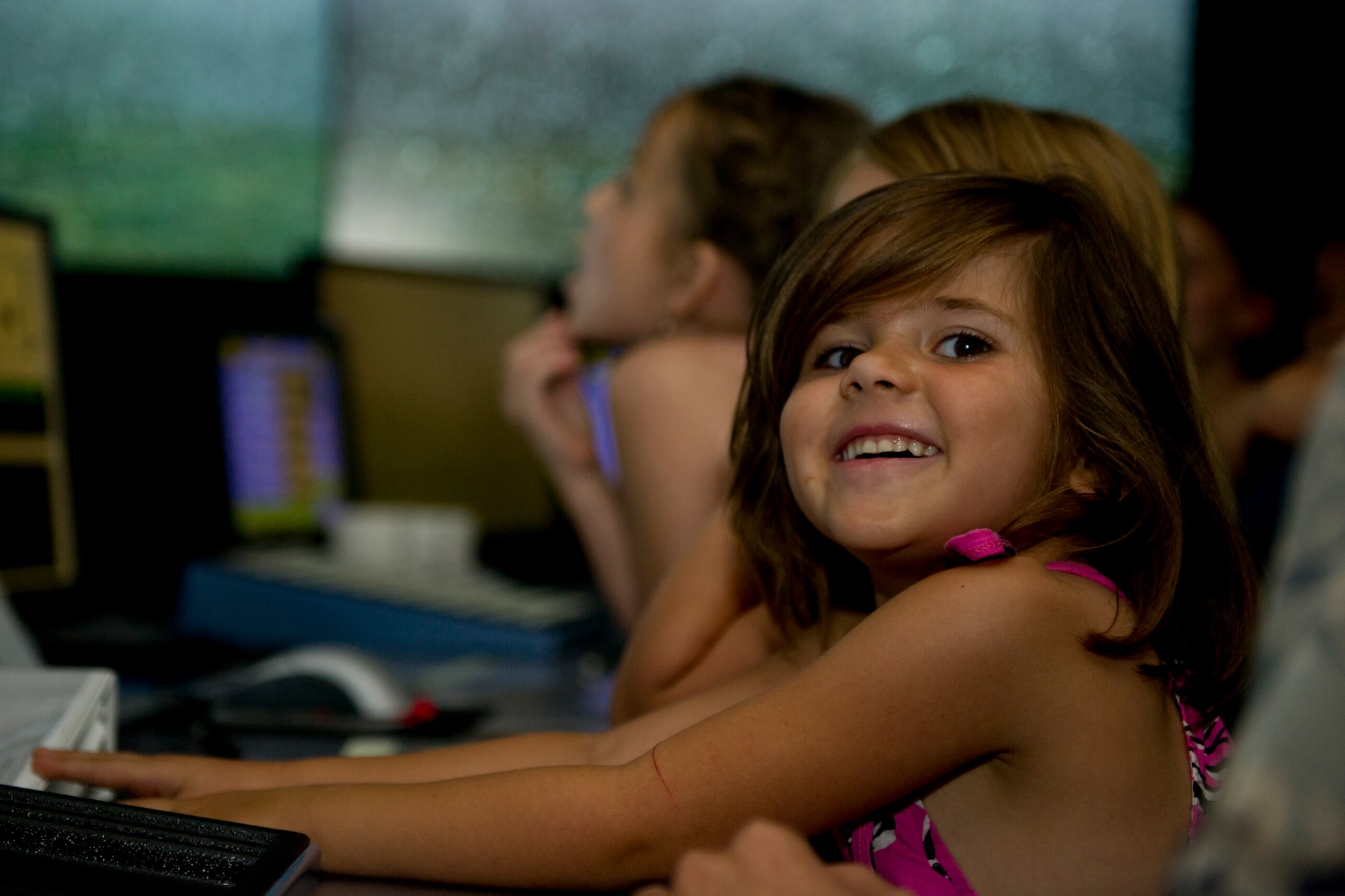 A child from the Youth Activities Center smiles as she watches her peers direct virtual aircraft on a training simulator in the air traffic control tower at Minot Air Force Base, N.D., July 24, 2015. After the training simulator, the children visited the control room on the top floor of the tower as the final stop on their tour. (U.S. Air Force photo/ Airman 1st Class Justin T. Armstrong)