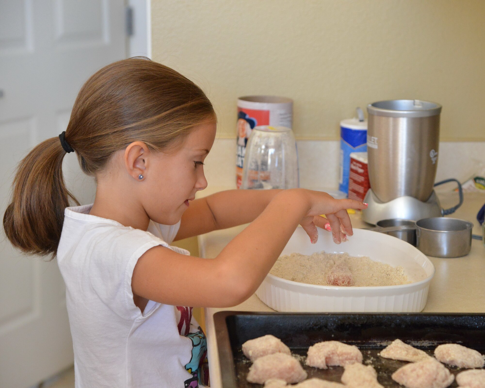 A young chef prepares chicken with a homemade batter during a “Cooking with Kids” class hosted by Kirtland Family Housing July 15. (Photo by Jamie Burnett)