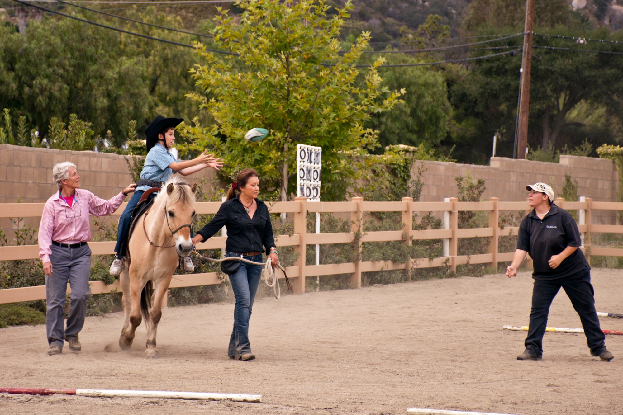 A special needs student catches a football from an instructor while participating in the Therapeutic Equestrian Program at the TERI “Campus of Life” in San Marcos, Calif., June 9, 2015. With the help of instructors, the modern horse takes on the role of therapist. For the student, program benefits include, increased strength and muscle tone, improved balance, flexibility, head control, and hand-eye coordination, as well as improved concentration and enhanced patience, self-esteem, and social awareness. (U.S. Air Force photo by Master Sgt. Jeff Walston)