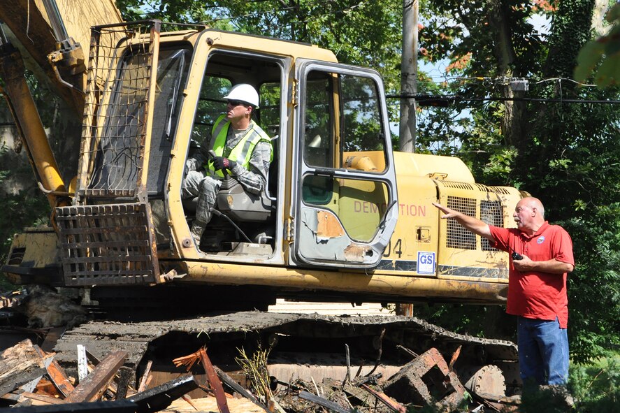 Tech. Sgt. Casey Klein, 910th Civil Engineer Squadron heavy equipment noncommissioned officer in charge, listens to instructions from City of Youngstown Street Department construction foreman Tom Sakmar while using an excavator to demolish a vacant, dilapidated house in the Taft School neighborhood on the city’s south side, July 23, 2015. Members of the 910th Civil Engineer Squadron, based at Youngstown Air Reserve Station teamed up with a City of Youngstown Street Department team to kick off a joint blight removal project to demolish at least a dozen blighted structures in this neighborhood under the Air Force Community Partnership Program. The program is designed to identify and develop mutually beneficial partnerships between Air Force installations and surrounding communities. In this case, the City of Youngstown gets skilled labor from the Civil Engineers, while the Civil Engineers gain valuable training opportunities that are hard to find under normal circumstances. (U.S. Air Force photo/Master Sgt. Bob Barko Jr.)