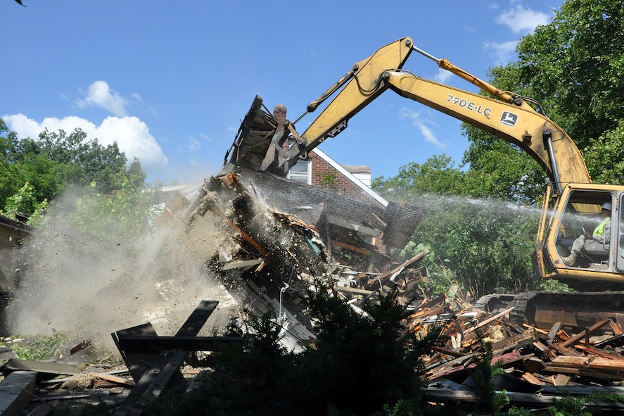 Tech. Sgt. Casey Klein, 910th Civil Engineer Squadron heavy equipment noncommissioned Officer in Charge, operates an excavator to bring down the remains of a vacant, dilapidated house while City of Youngstown Street Department workers spray the pieces with water to keep dust and debris out of the air during the work being done in the Taft School neighborhood on the south side here, July 23, 2015. Members of the 910th Civil Engineer Squadron, based at Youngstown Air Reserve Station, teamed up with a City of Youngstown Street Department team to kick off a joint blight removal project to demolish at least a dozen blighted structures in this neighborhood under the Air Force Community Partnership Program. The program is designed to identify and develop mutually beneficial partnerships between Air Force installations and surrounding communities. (U.S. Air Force photo/Master Sgt. Bob Barko Jr.)