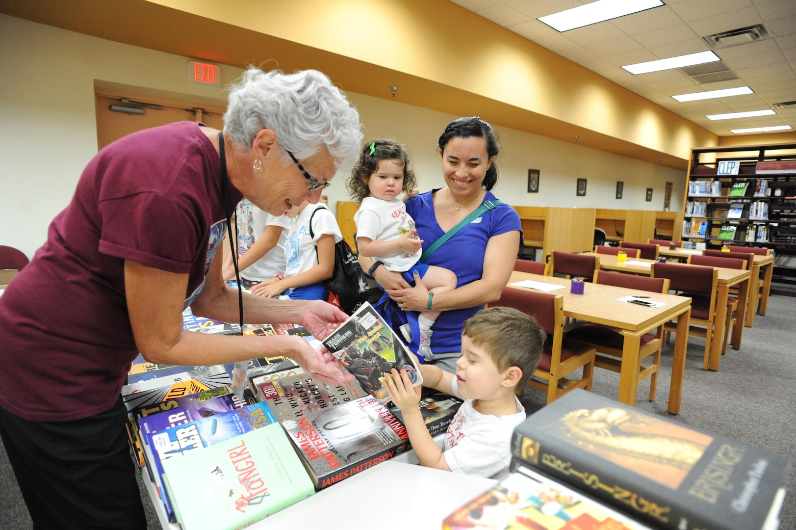 Robin Miller, Joint Base San Antonio-Randolph Library volunteer, hands a book to Alex Auger July 22 at the JBSA-Randolph Library.