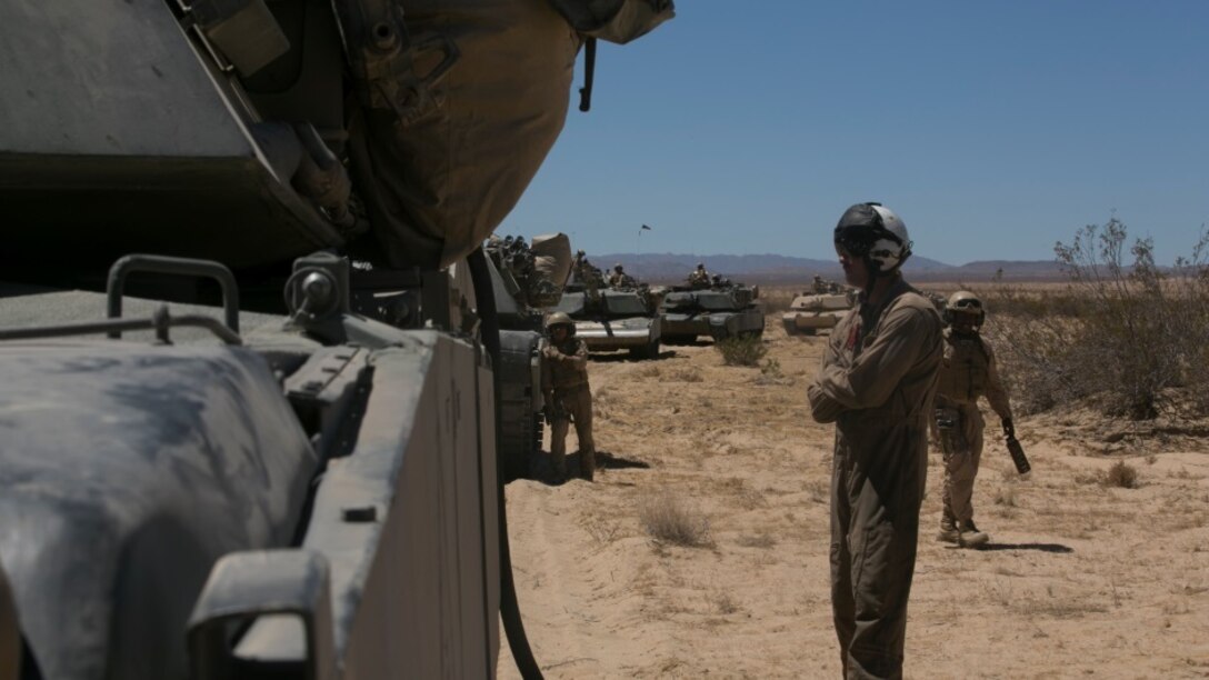 Sgt. Brandon Crist, crew chief, Marine Heavy Helicopter Squadron 465 waits by an M1A1 Abrams Tanks during a refueling exercise at Acorn Training Area, July 16, 2015. 1st Tanks conducted the exercise during their company’s gunnery examination. (Official Marine Corps photo by Lance Cpl. Thomas Mudd/Released)