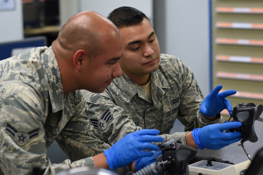 Airman 1st Class Raymundo Leija and Senior Airman Kenny Batallas, both 374th Operations Support Squadron aircrew flight equipment journeymen, inspect the mask of a flight helmet at Yokota Air Base, Japan, July 29, 2015. The AFE Airmen broke down, cleaned and inspected every part of the helmet to make sure everything was in working order. (U.S. Air Force photo by Senior Airman Michael Washburn/Released)