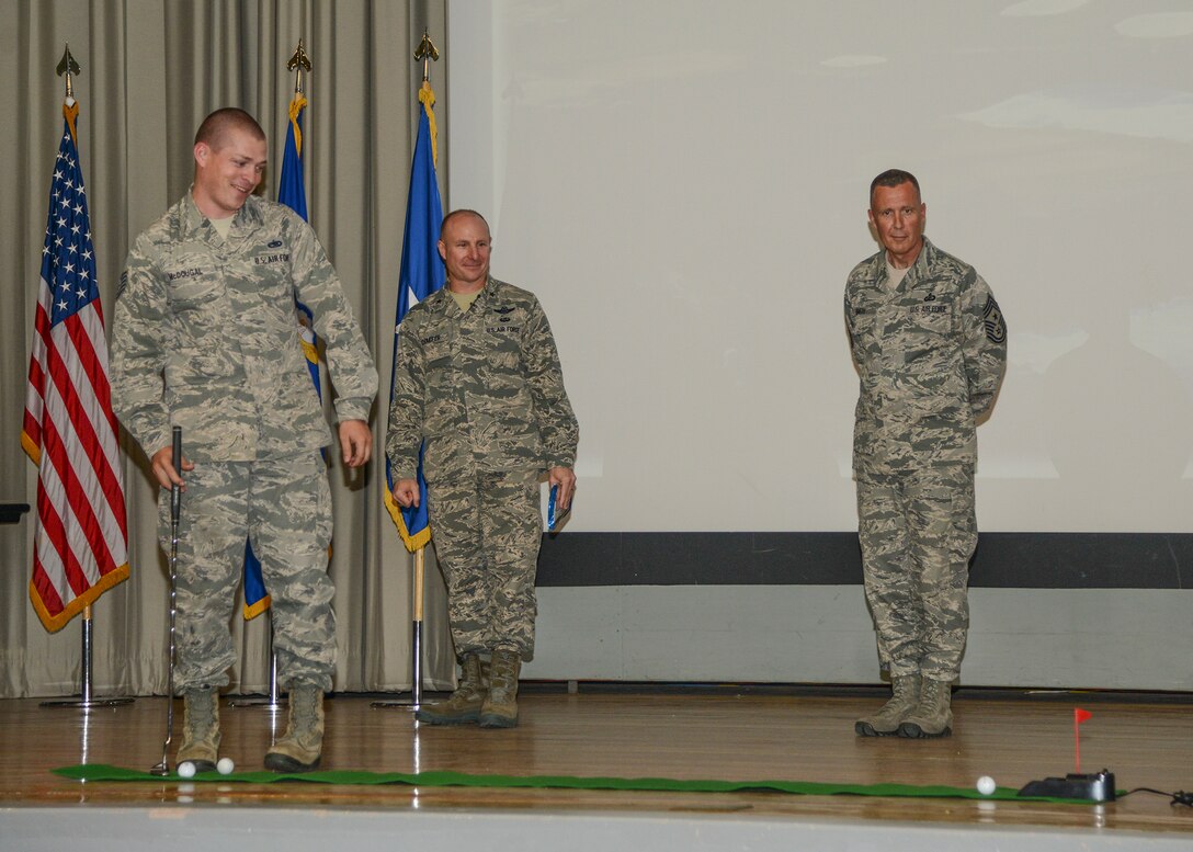 Staff Sgt. Kirk McDougal, 412th Maintenance Group, putts a golf ball on stage during the quarterly awards ceremony July 30, at the base theater. McDougal was named Honor Guard of the Quarter. His award was presented by Brig. Gen. Carl Schaefer (center), 412th Test Wing commander and Chief Master Sgt. David Smith (right), 412th Test Wing command chief. (U.S. Air Force photo by Rebecca Amber)