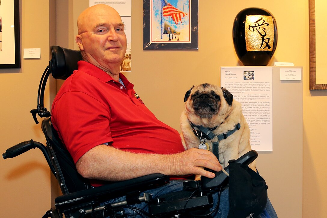 Jim Russell sits in the middle of the The Janice Griffiths Gallery with his rotund service pug, Mr. Beau, resting on his lap. The dim lights and cool interior of the gallery offer both some relief from the heat of the day as Russell recounts his tale of his life journey from military discipline to artistic expression.  