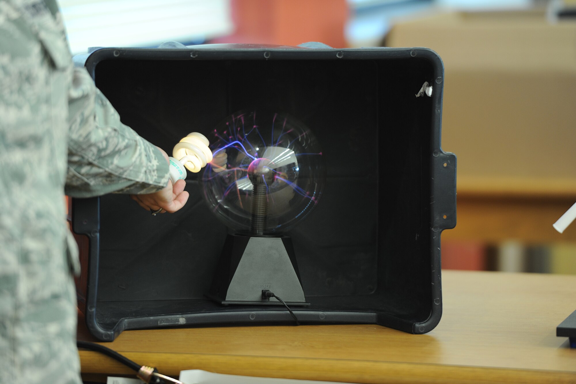 U.S. Air Force Staff Sgt. Natasha M. Mattoon, 312th Training Squadron special instruments training instructor, demonstrates how a plasma sphere can light up a florescent light bulb at the Consolidated Learning Center, Goodfellow Air Force Base, Texas, July 28, 2015. Other items used included an earthquake table, Slinky, interior model globe of the earth, and florescent light bulb. (U.S. Air Force photo by Staff Sgt. Laura R. McFarlane/ Released)