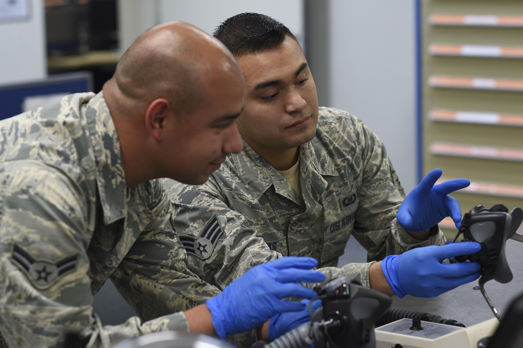 U.S. Air Force Airman 1st Class Raymundo Leija and Senior Airman Kenny Batallas, both 374th Operations Support Squadron aircrew flight equipment journeymen, inspect the mask of a flight helmet at Yokota Air Base, Japan, July 29, 2015. The AFE Airmen broke down, cleaned and inspected every part of the helmet to make sure everything was in working order. (U.S. Air Force photo by Senior Airman Michael Washburn/Released)
