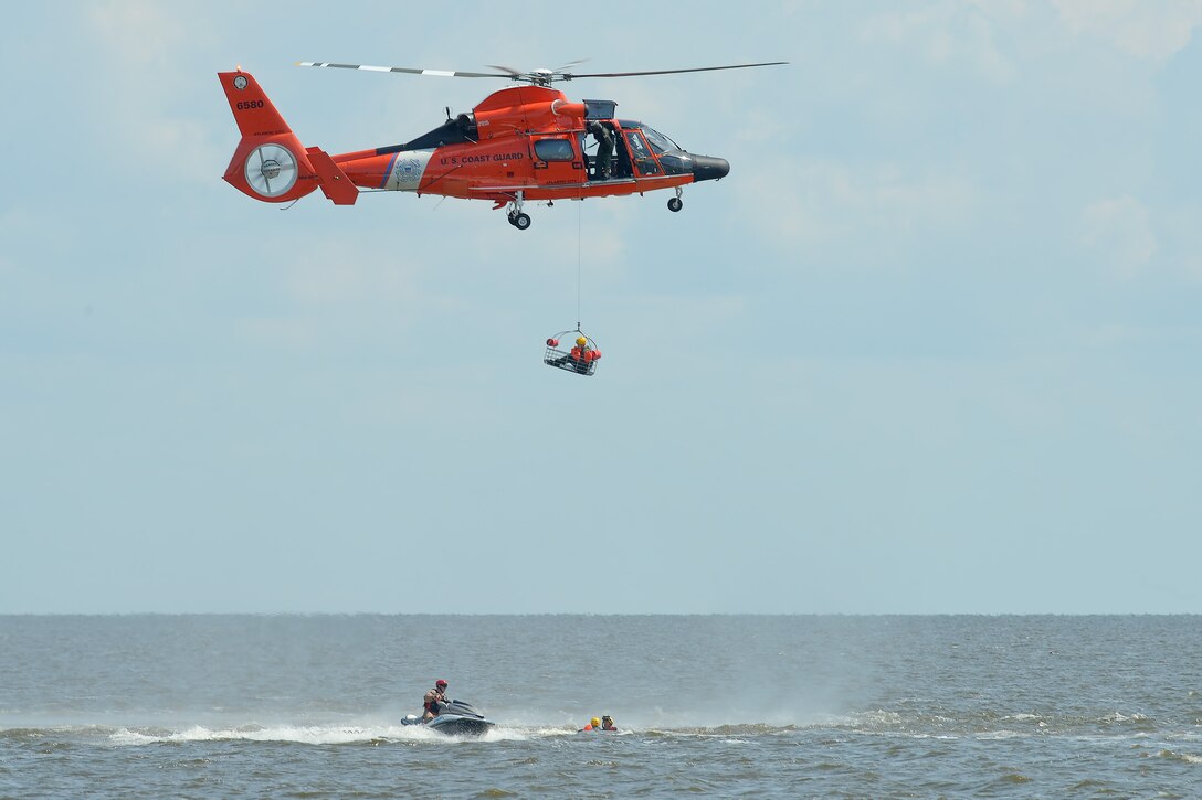 A Coast Guard HH-65D Dolphin practices hoisting Air Force aircrew members while a Coast Guard rescue swimmer prepares the next student, who was just moved into position by Staff Sgt. Adam Ellerd, the 436th Operations Support Squadron Survival, Evasion, Resistance and Escape Operations NCO in charge, using a personal watercraft July 17, 2015, near Dover Air Force Base, Del. The HH-65D is based at Coast Guard Air Station Atlantic City, N.J. (U.S. Air Force photo/Greg L. Davis)