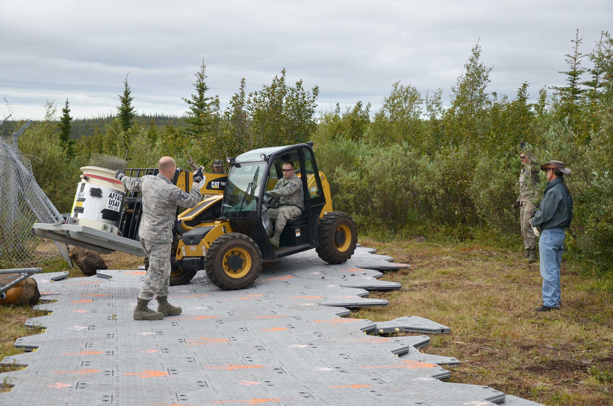 Master Sgt. Kevin Sanger (left) spots forklift driver Tech. Sgt. Larry Bouchard, both with the Air Force Technical Applications Center's Detachment 460 at Eielson AFB, Alaska, as Bouchard carefully transports a radioisotope thermoelectric generator from its trailer to an awaiting CH-47 Chinook July 17, 2015, for transport back to Eielson, while project manager Scott Lattimer (far right) observes.  The RTGs, which contain radiologic material, were originally used because of their high reliability and low maintenance requirements to determine if regional seismic activity was caused by nuclear explosions or naturally-occurring events such as earthquakes, mining explosions, volcanic activity, etc.  AFTAC’s primary mission is to verify compliance with nuclear test ban treaties.  (U.S. Air Force photo by Susan A. Romano)