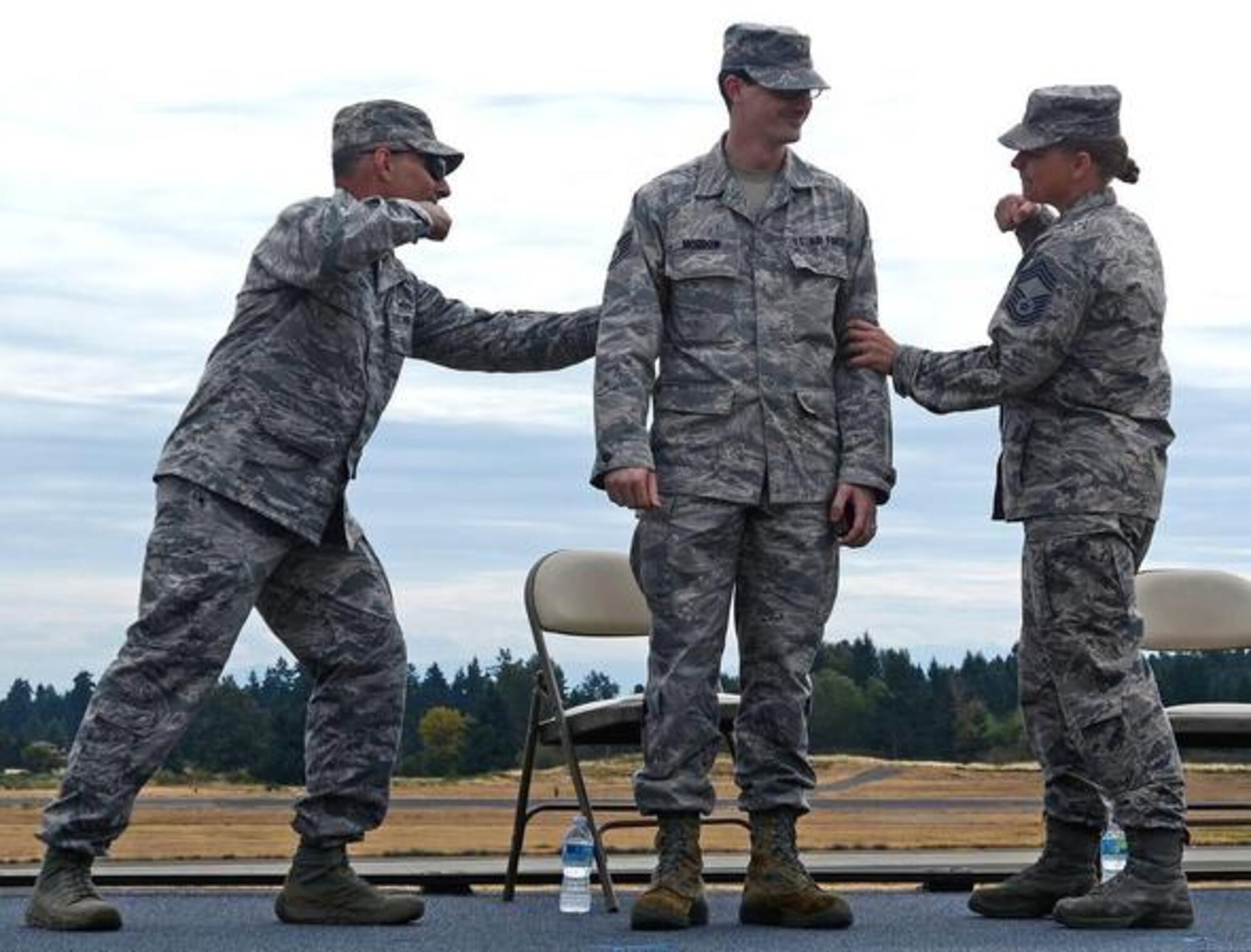 Col. Anthony Davit (left), and Chief Master Sgt. Kristen Orcutt, tack on the stripes for Staff Sgt. Christopher Morrow on his promotion during a unit farewell commander’s call and barbecue July 24 at McChord Field. (Northwest Guardian photo by Senior Airman Jacob Jimenez)