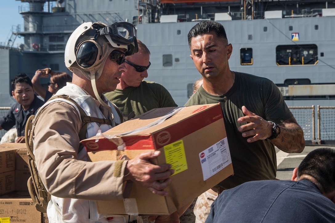 U.S. Marine Lt. Col. Wilfred Rivera, left, passes supplies to Staff Sgt. Sean Newman during replenishment at sea aboard the USS Rushmore (LSD 47) at sea in the Pacific Ocean, May 31, 2015. Rivera is the commanding officer of Combat Logistics Battalion 15, 15th Marine Expeditionary Unit and Newman is a section leader with Kilo Company, Battalion Landing Team 3rd Battalion, 1st Marine Regiment, 15th Marine Expeditionary Unit. Marines and Sailors worked together to off load supplies and mail from loved ones. (U.S. Marine Corps photo by Sgt. Emmanuel Ramos/Released)