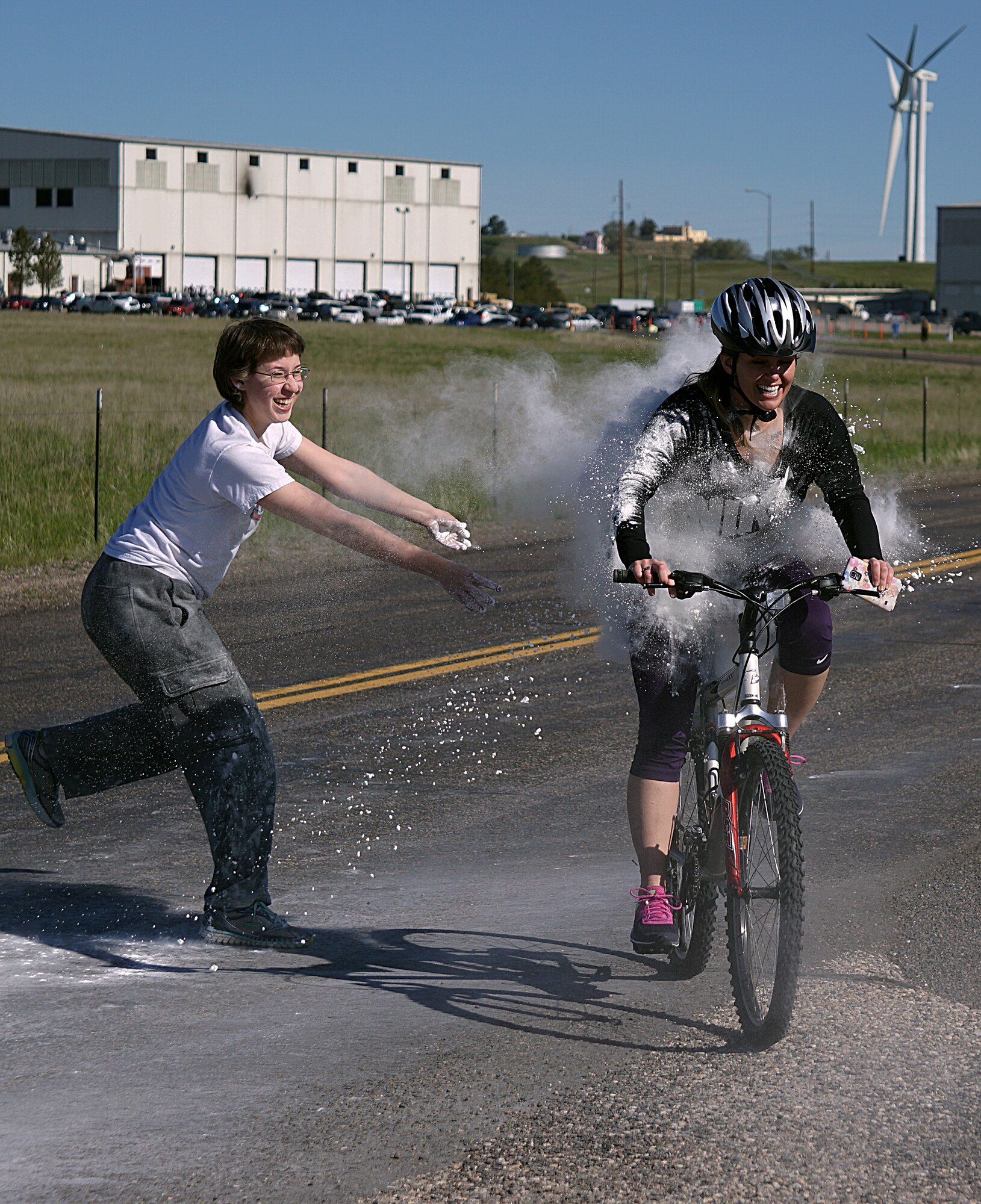 Airman 1st Class Lelaini Rinker, 90th Missile Maintenance Squadron, throws a handful of white corn starch at Airman 1st Class Emilee Edelman, 90th Comptroller Squadron finance costumer service technician, during the Air Force Sergeant’s Association 5-kilometer Color Run. Edelman, who rode at the end of the race for safety purposes, learned that even volunteers weren’t safe from being blasted with colors. (U.S. Air Force photo by Airman 1st Class Brandon Valle)