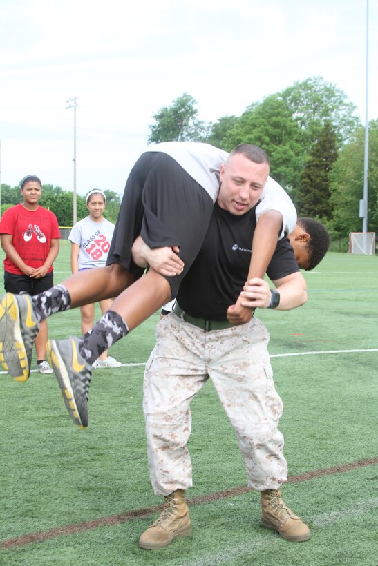 U.S. Marine Corps Sgt. Michael A. DeCamilla Jr., recruiter for Recruiting Sub-station Leesburg and native of Rochester, New York, demonstrates how to properly execute a fireman carry May 19, 2015, at Herndon High School in Herndon, Virginia. Throughout the day, DeCamilla and other Marines multiple of students through a series of physically demanding exercises including ammunition-can lifts, squad pushups and relay races. (U.S. Marine Corps photo by Sgt. Anthony Kirby/Released)