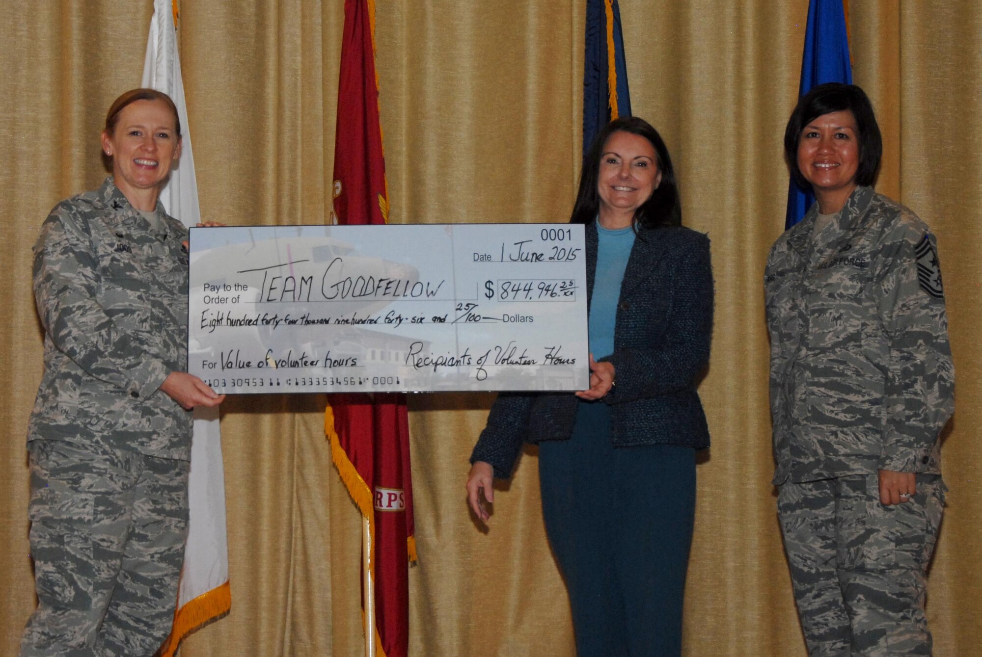 Jane L. Mickenheim, 17th Force Support Squadron Airman and Family Readiness chief, presents U. S. Air Force Col. Kimberlee P. Joos, 17th Training Wing Commander, and Chief Master Sgt. JoAnne S. Bass, 17th TRW Command Chief, with a check for $844,946.25 during a volunteer recognition event at the base theater on Goodfellow Air Force Base, Texas, June 1, 2015. Mickenheim used the check to represent the amount the community saved from Goodfellow volunteers. (U.S. Air Force photo by Senior Airman Joshua Edwards/Released)
