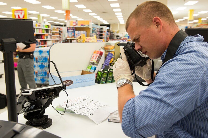 Inspector William Terpestra, 23d Security Forces Squadron, photographs the crime scene during an anti-robbery exercise at the Exchange June 1, 2015, at Moody Air Force Base, Ga. Senior investigators evaluated Terpestra’s ability to secure the crime scene, photograph evidence, interview the witness and gather fingerprints to assist in the investigation. (U.S. Air Force photo by Airman 1st Class Ceaira Tinsley/Released)